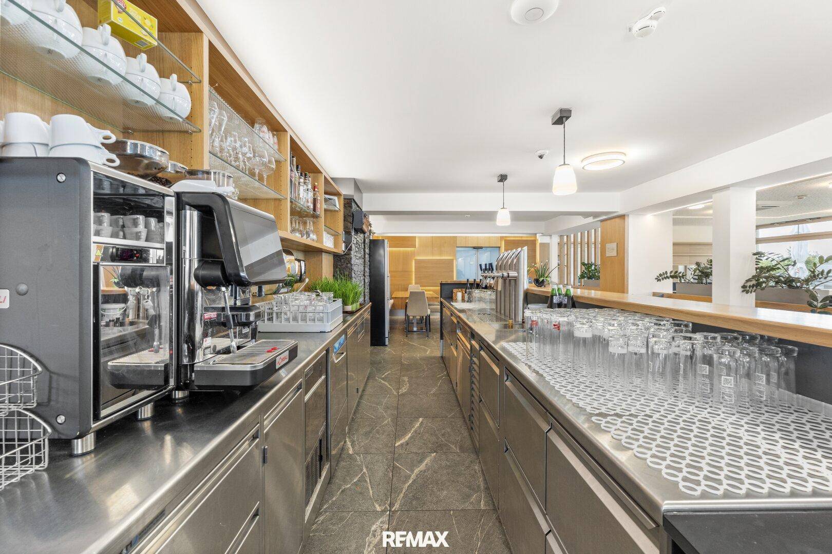 Weitere Ansicht hinter der Bar mit Kaffeemaschine, Gläsern und Flaschen in den Regalen für den Betrieb.