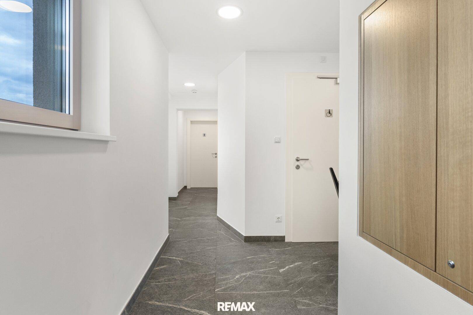 Heller Flur mit weißen Wänden, modernen Fliesen und Holztüren, durch ein Fenster belichtet.