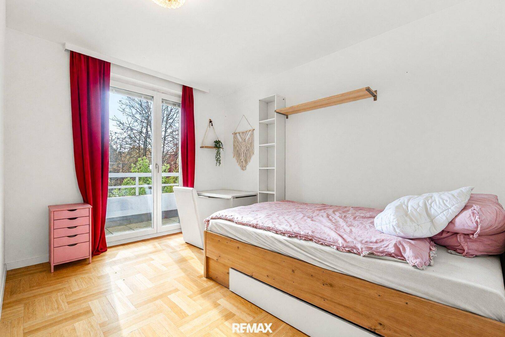Kinderzimmer mit Parkettboden, Zugang zum Balkon und farbigen Vorhängen.