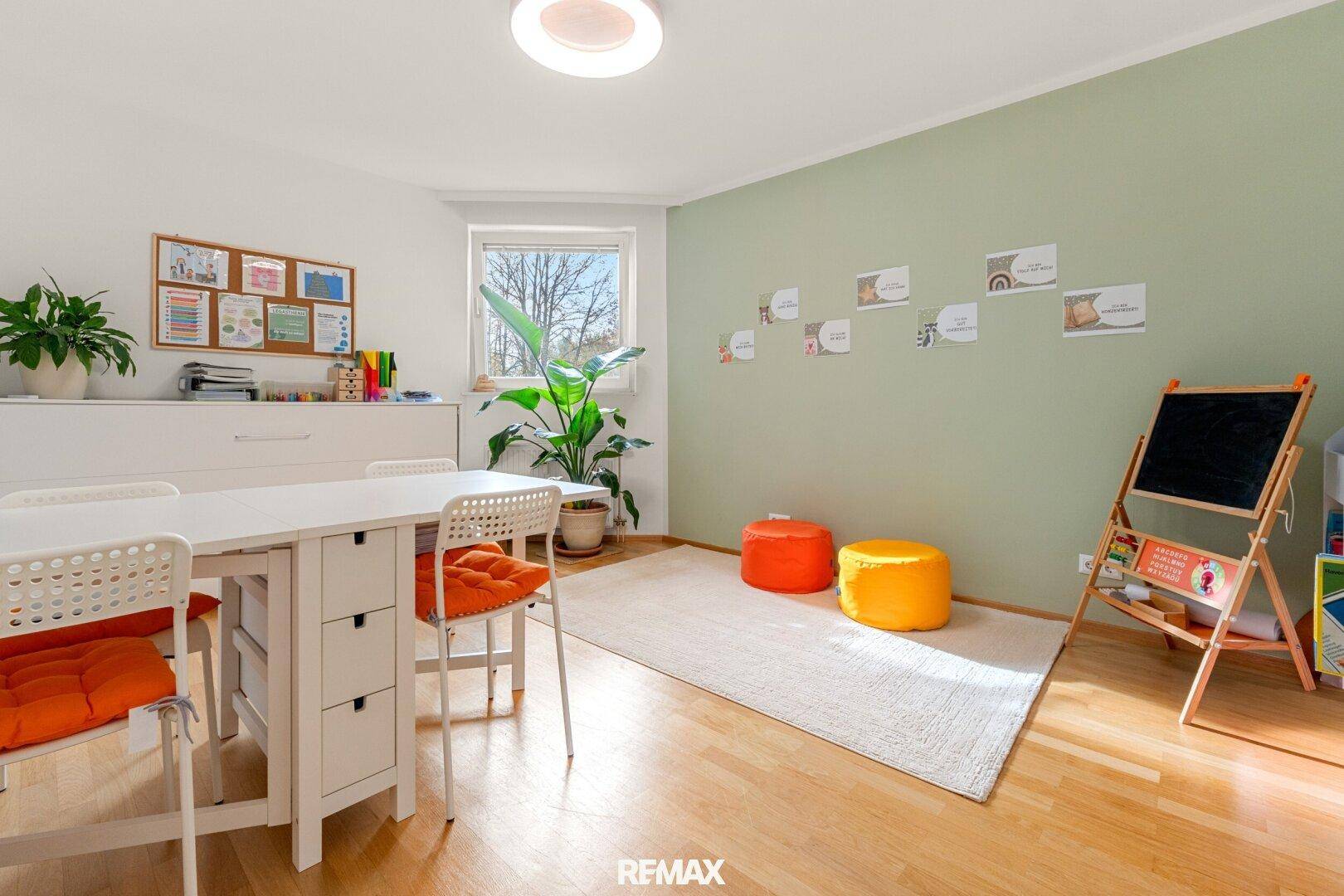 Helles Arbeits- oder Spielzimmer mit Holzboden, grüner Akzentwand und viel Tageslicht.