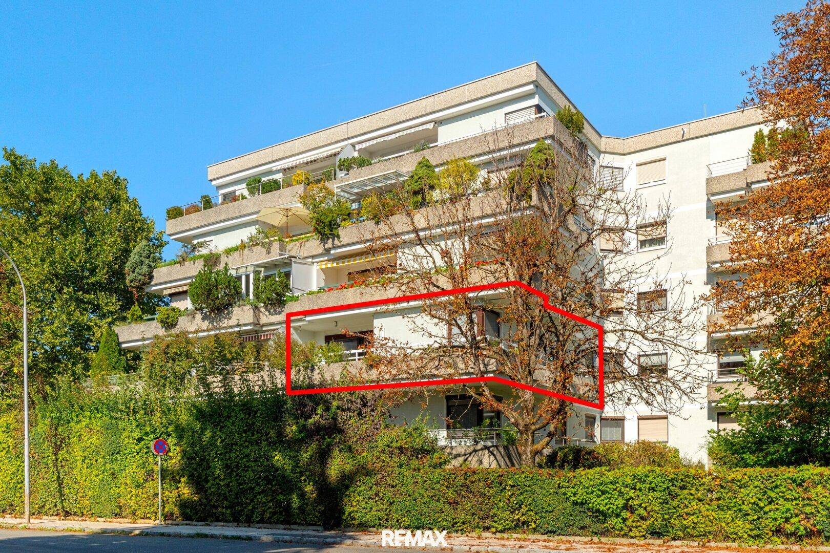 Mehrfamilienhaus mit begrünten Balkonen und umgebender Hecke.