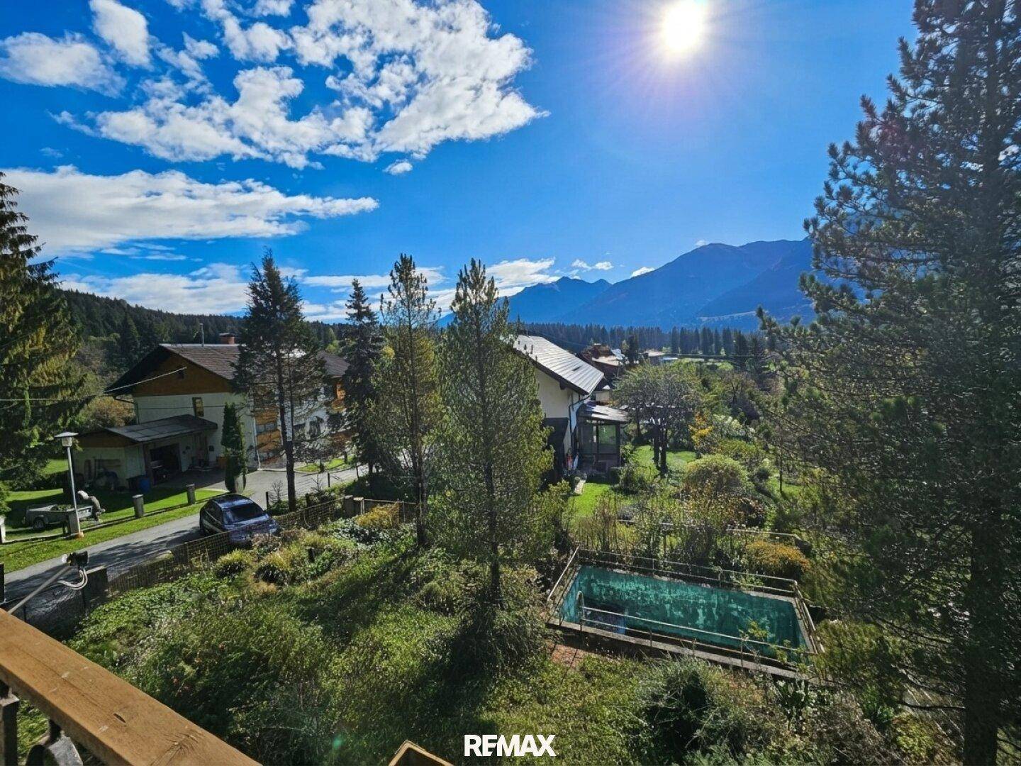 Weitläufiger Blick über die Landschaft mit Bergen, einem Pool und umliegenden Häusern unter blauem Himmel.