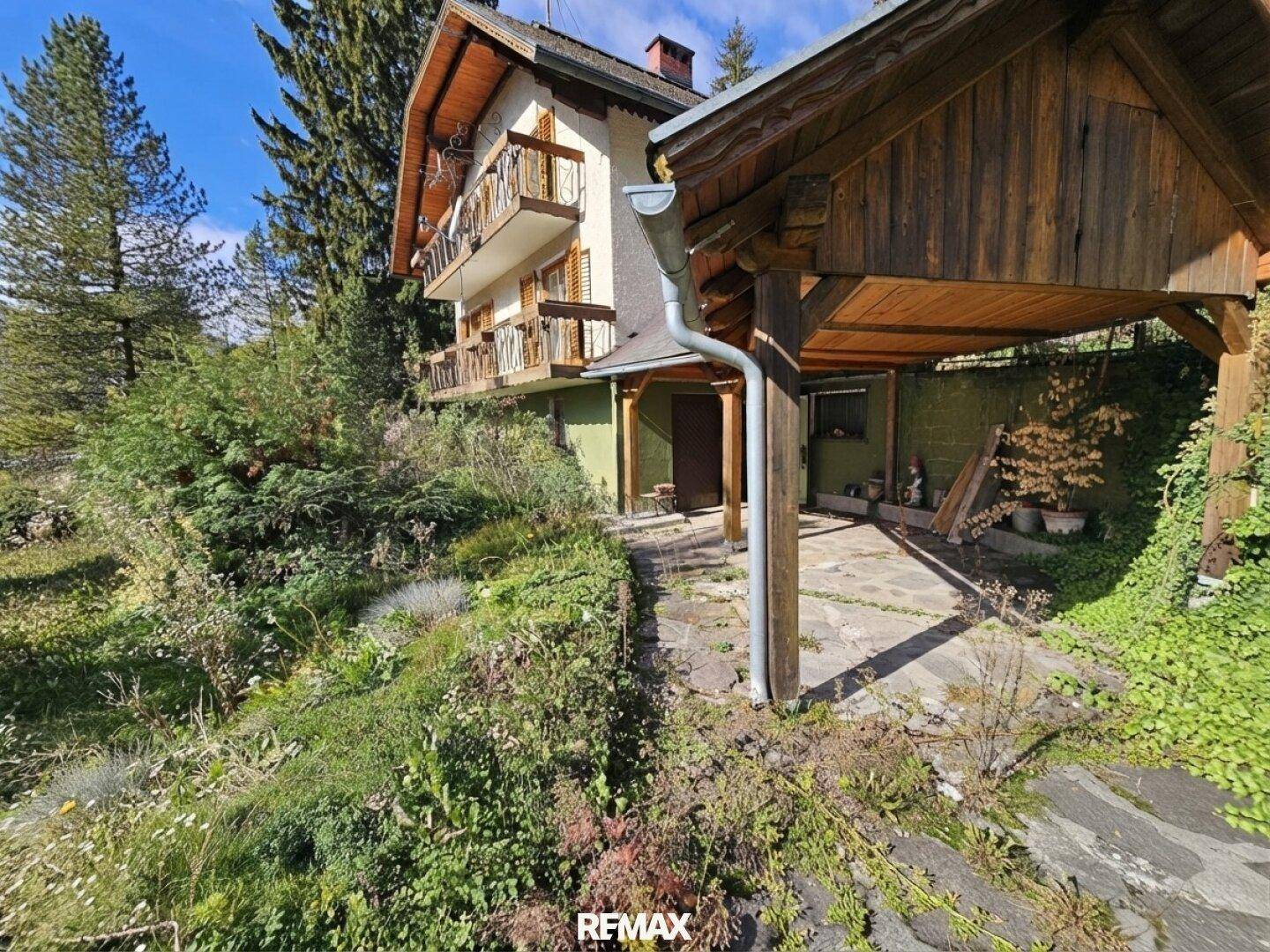 Seitenansicht des Hauses mit überdachtem Carport und Zugang zum Eingang, umgeben von Vegetation.