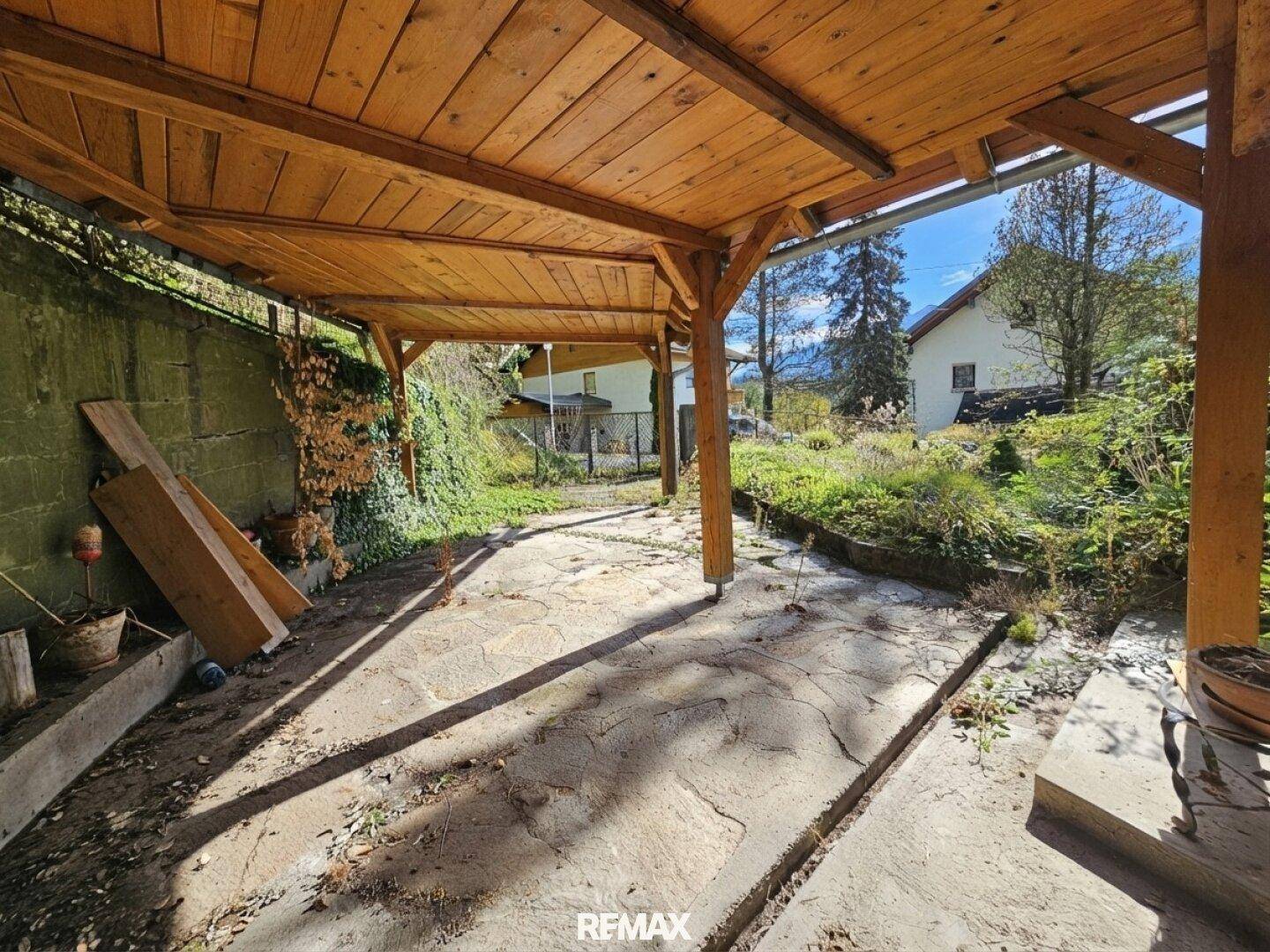 Geräumiger, überdachter Carport mit Holzdach und Steinboden, bietet Schutz für Fahrzeuge.