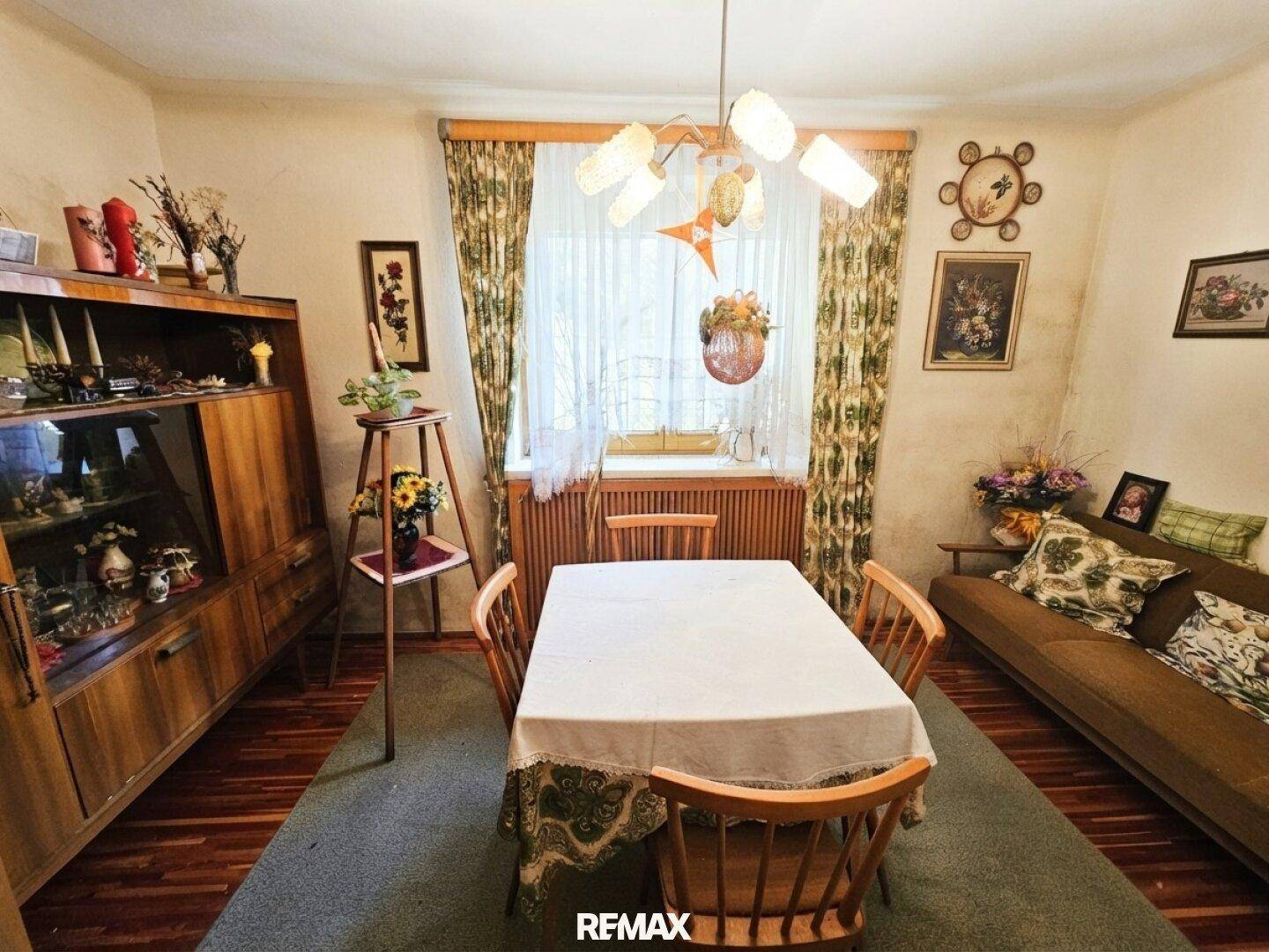 Traditioneller Essbereich mit Holztisch und Stühlen, umgeben von floralen Vorhängen und einem Teppich.