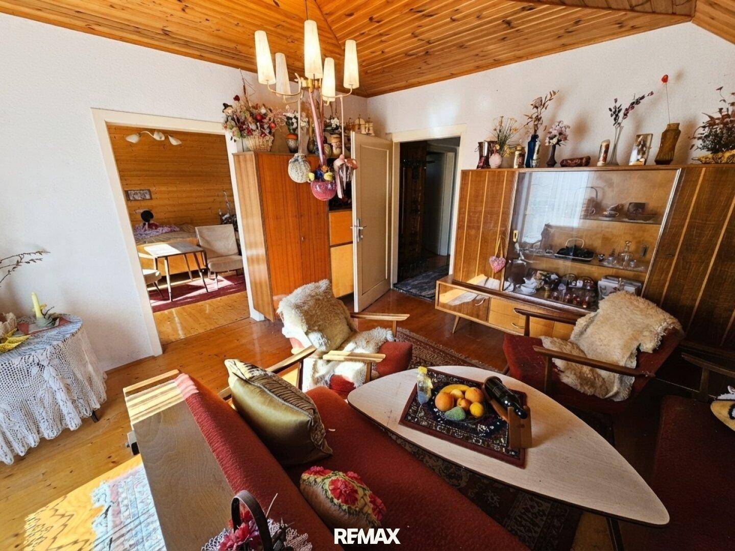 Helles Wohnzimmer mit Holzbalkendecke, Vintage-Möbeln und Blick in einen weiteren Raum.