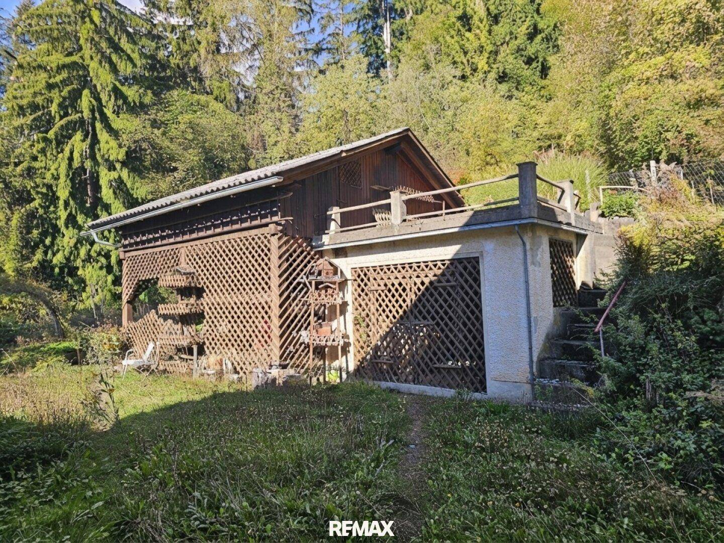 Nebengebäude mit Holzverkleidung und einer kleinen Terrasse, umgeben von üppigem Grün.