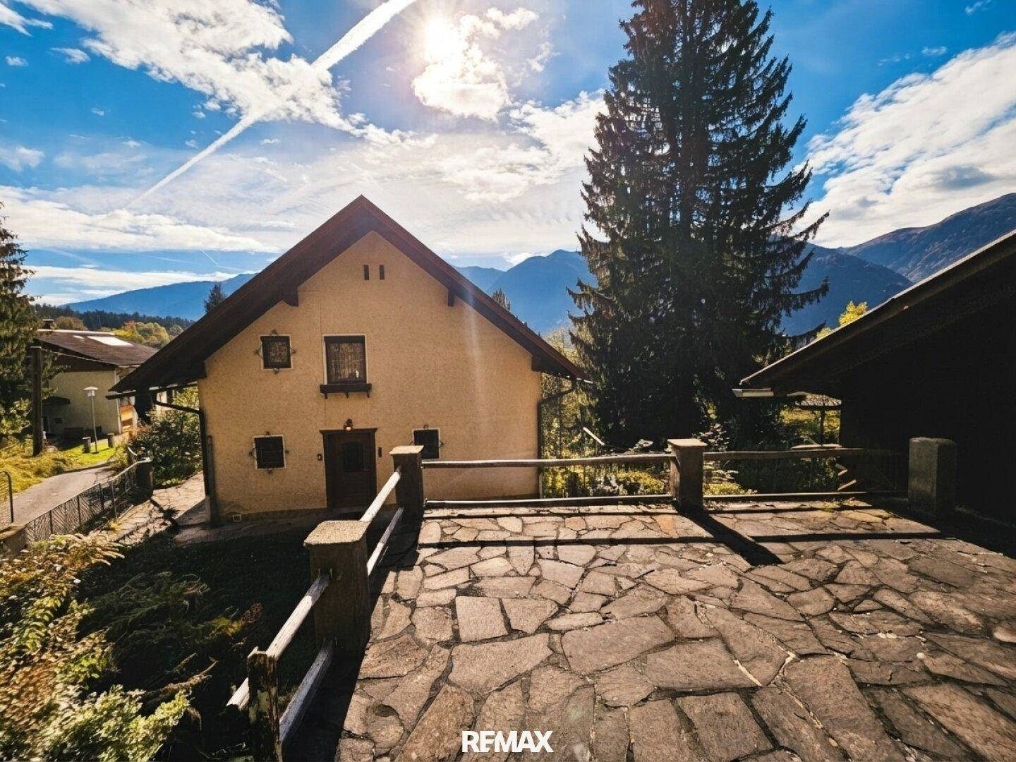 Große Steinterrasse mit Blick auf das Haus und die umliegende Berglandschaft unter blauem Himmel.