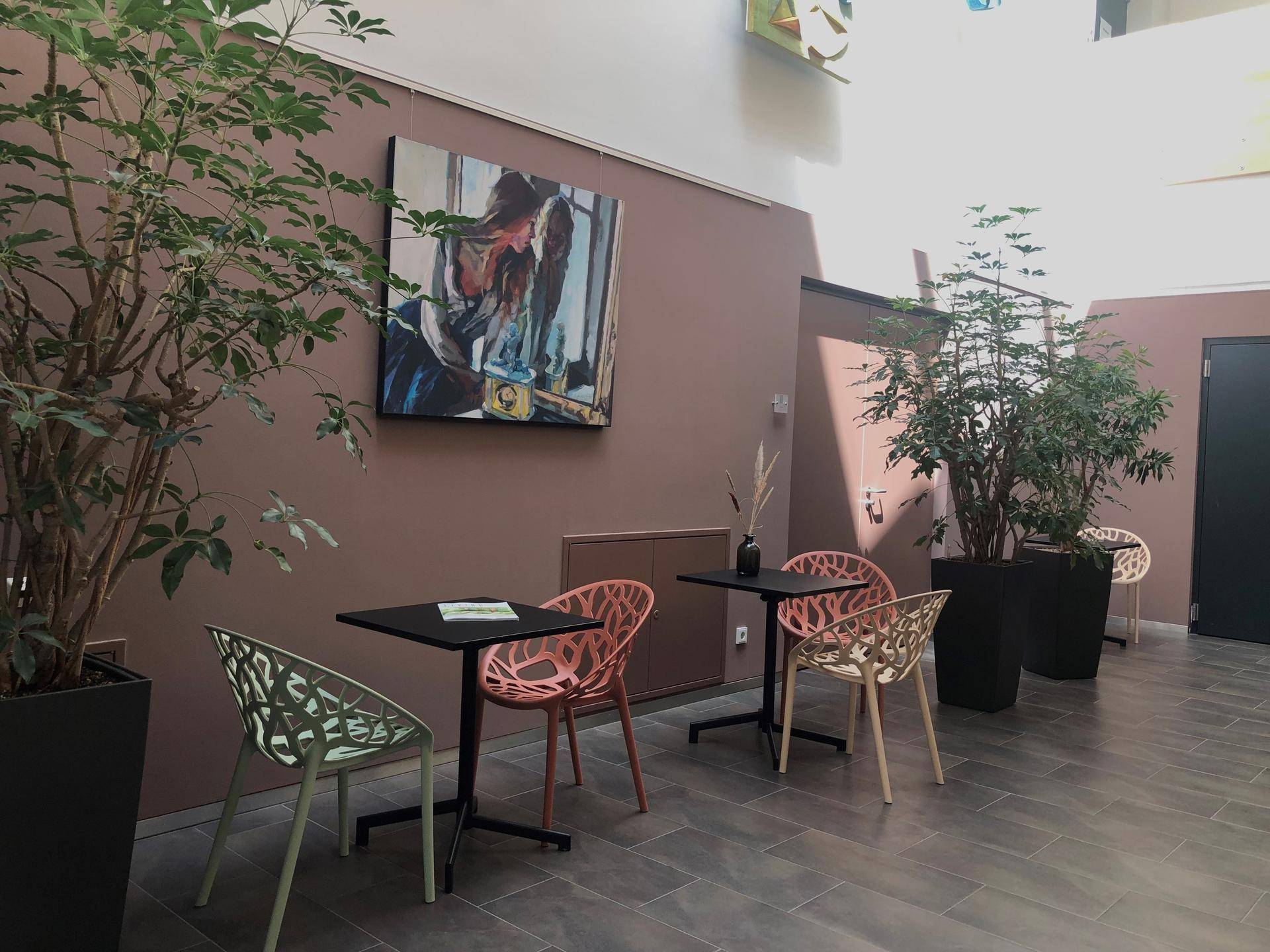 Gemütlicher Loungebereich mit kleinen Tischen, modernen Stühlen, großen Pflanzen und Kunstwerken an der Wand.