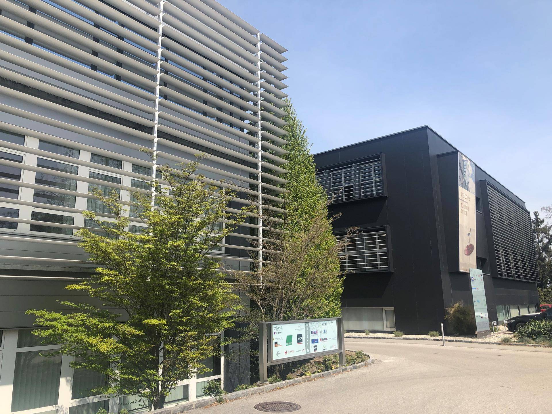 Zwei moderne Bürogebäude mit unterschiedlichen Fassadenstrukturen und viel Grün in der Umgebung.