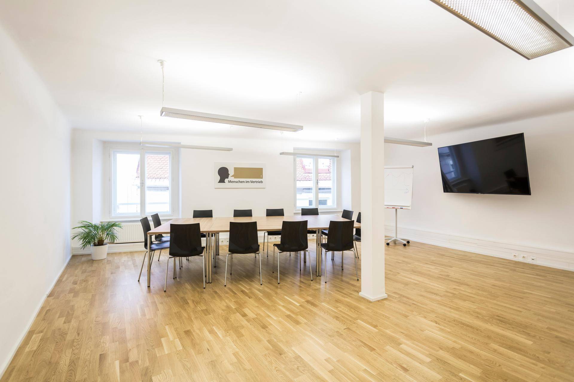 Geräumiger Konferenzraum mit langem Holztisch, vielen Stühlen und einem großen Wandfernseher.