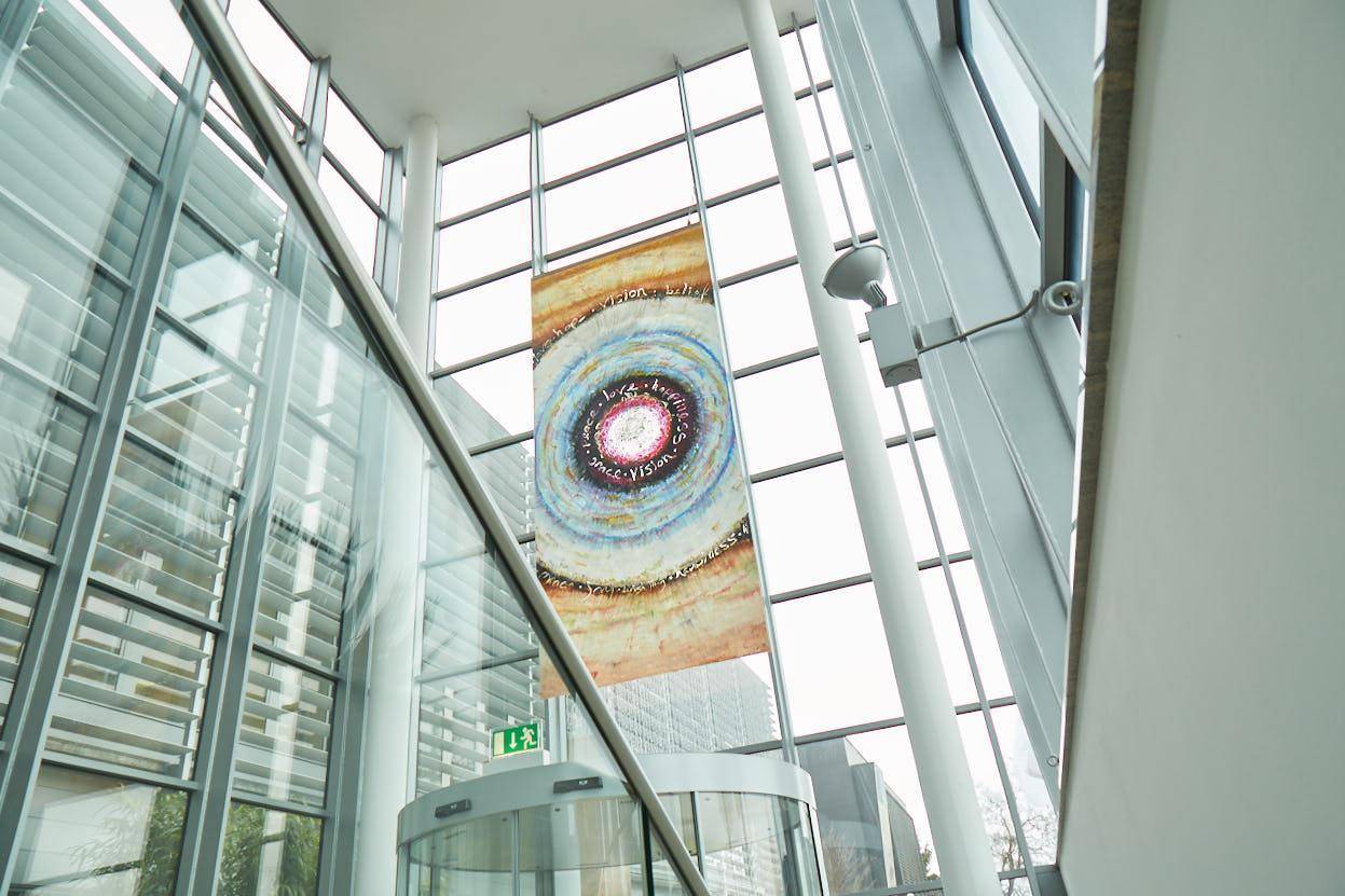 Helle Lobby mit hoher Glasfassade und einem großen, farbenfrohen Banner.
