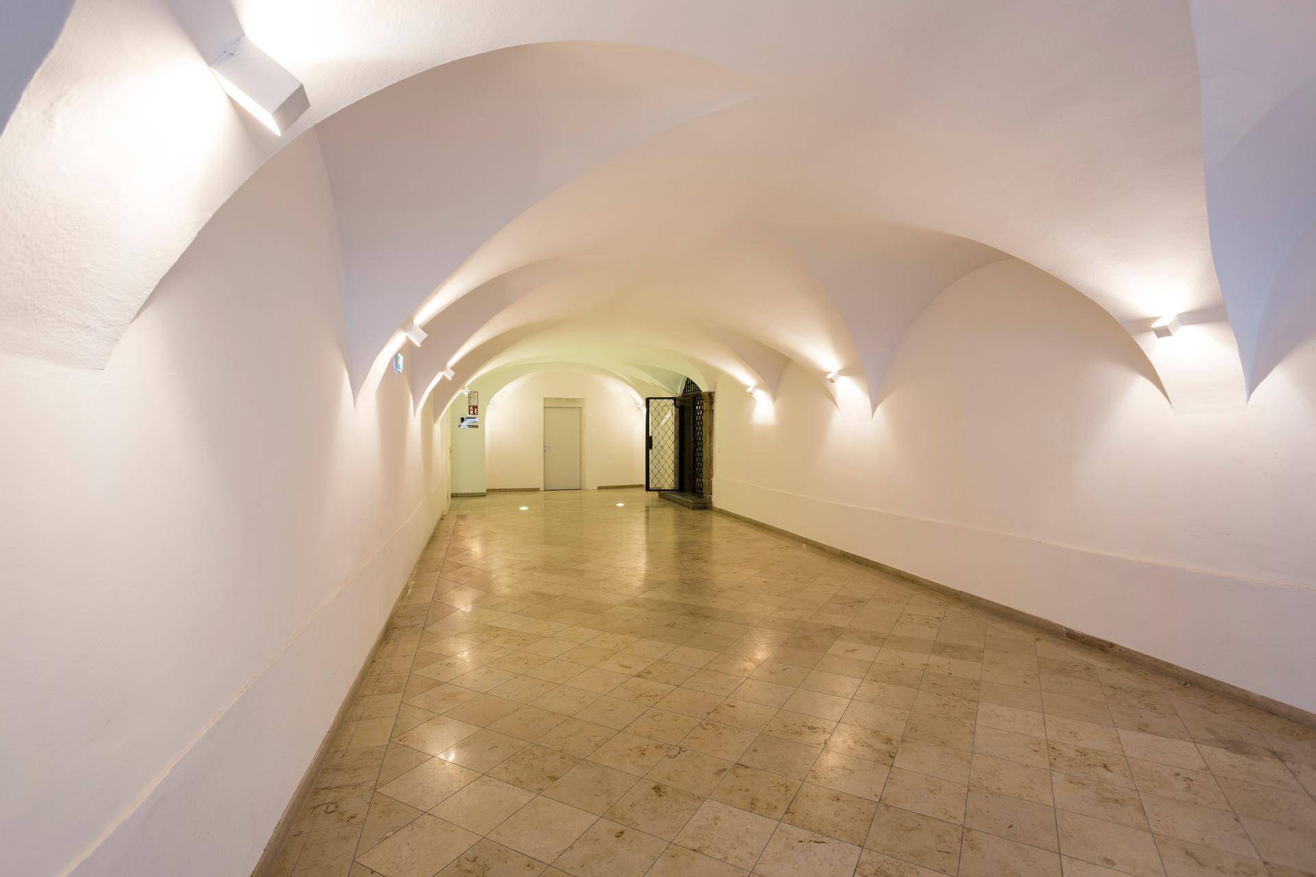 Langer, heller Flur mit gewölbter Decke und glänzendem Marmorboden, beleuchtet von Wandleuchten.