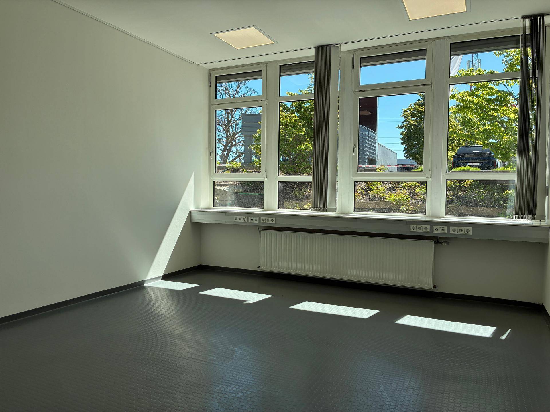 Leerer Büroraum mit großen Fenstern, die viel Sonnenlicht hereinlassen und einen Blick auf die Umgebung ermöglichen.