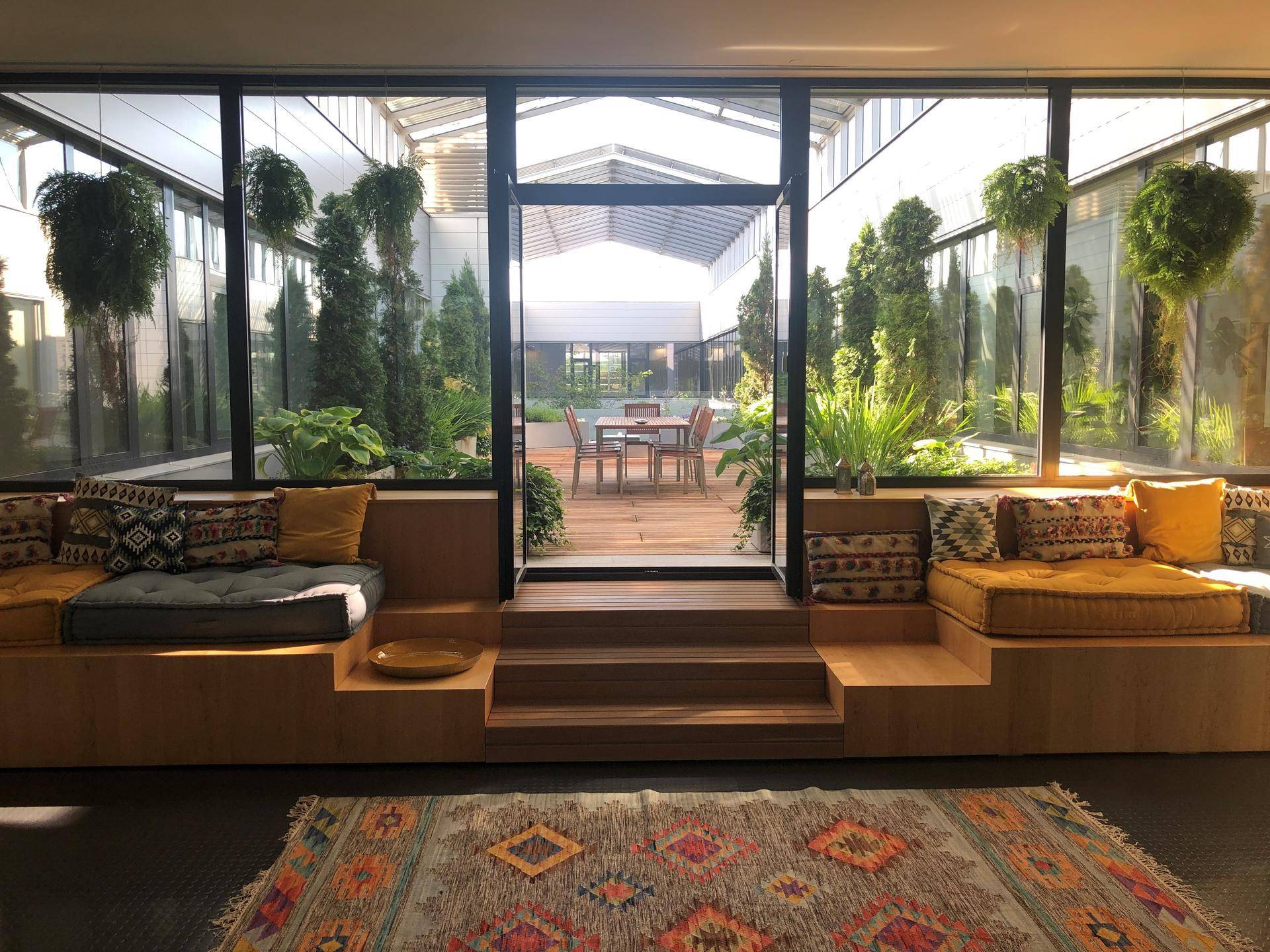 Heller Loungebereich mit bequemen Sitzgelegenheiten und Blick auf einen begrünten Innenhof durch große Glasfronten.