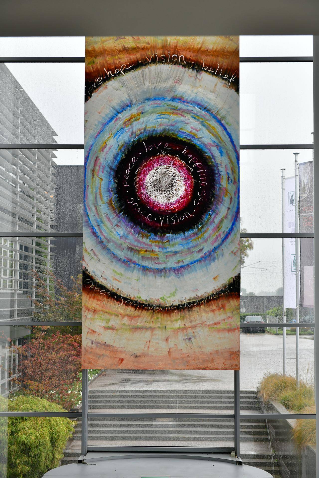 Großes Kunstwerk in einem hellen Flur mit großen Fenstern, das eine lebendige Atmosphäre schafft.