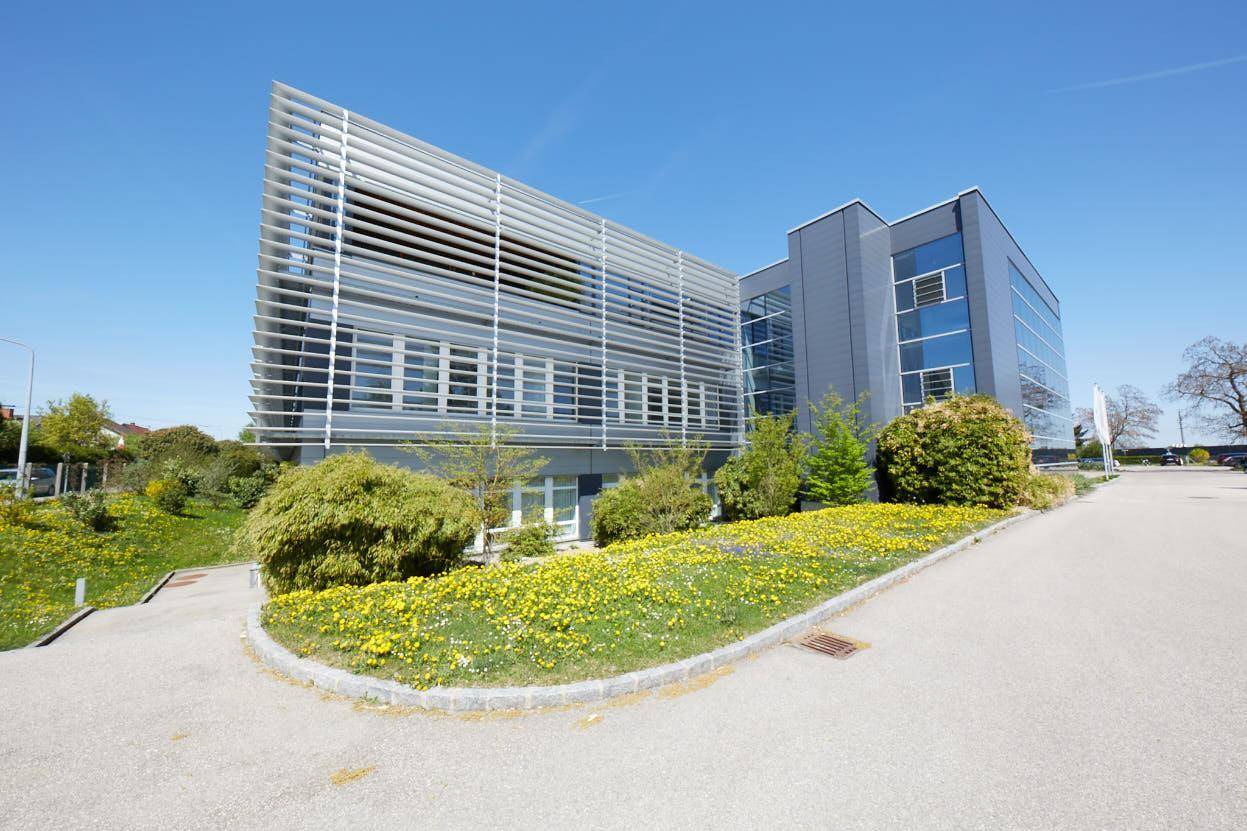 Modernes Bürogebäude mit markanter Lamellenfassade, umgeben von gepflegten Grünflächen und einer Zufahrt.
