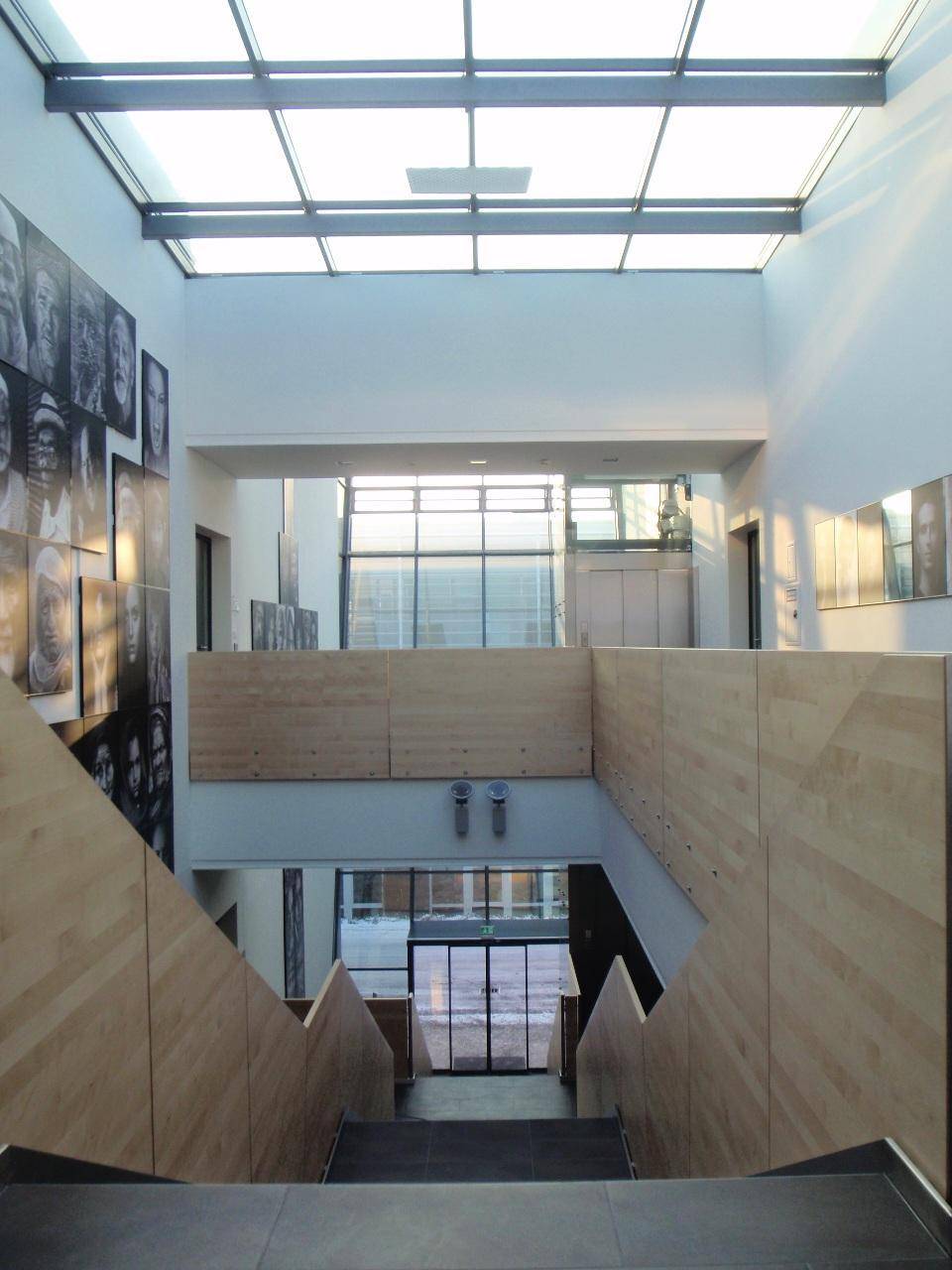 Hohes Atrium mit Holzverkleidung, Treppen und Oberlichtern, die den Raum mit natürlichem Licht füllen.