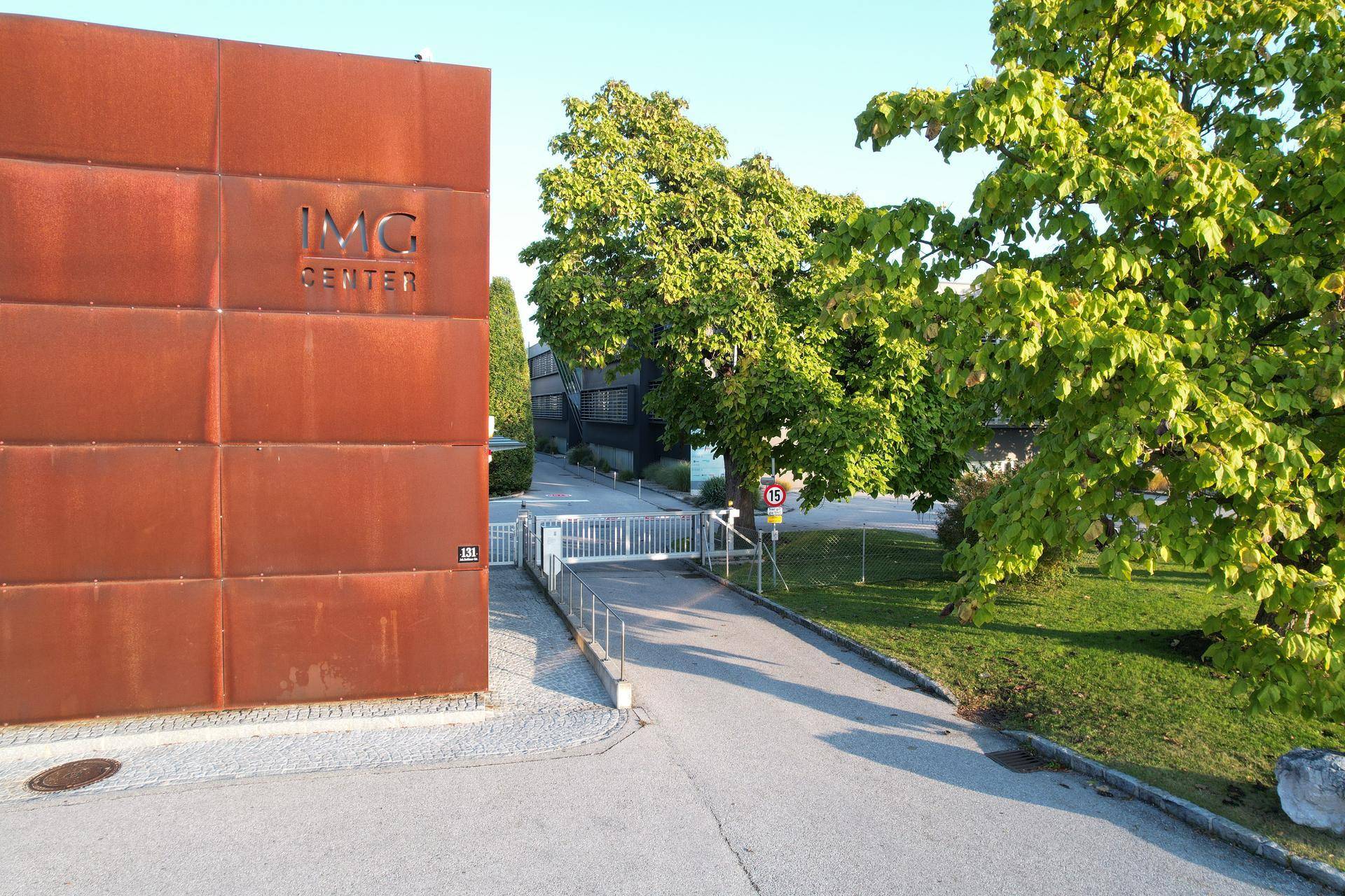 Eingangsbereich eines modernen Gebäudes mit rostfarbener Fassade und grüner Umgebung.