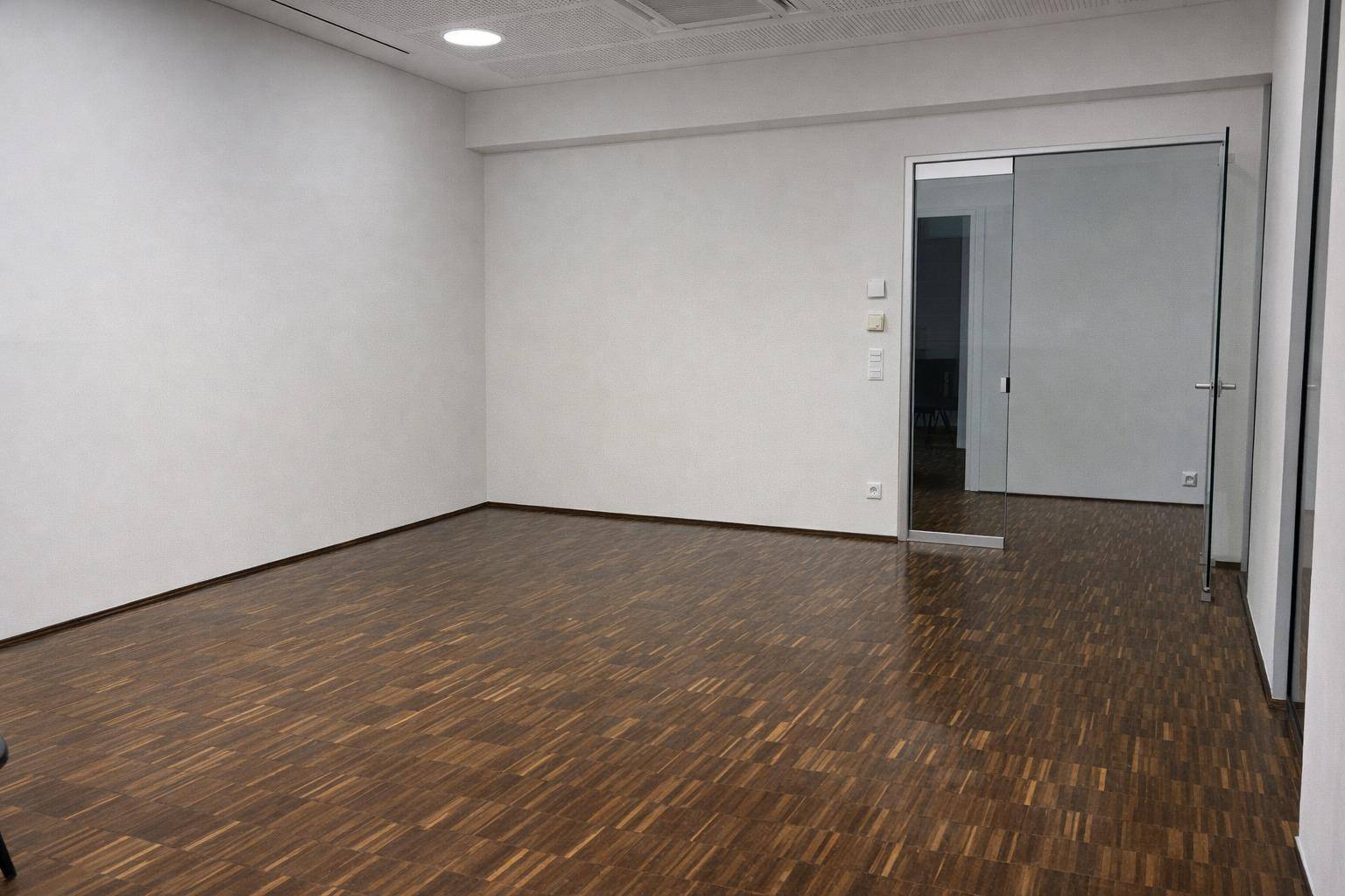 Leeres Büro mit Holzboden und einer Glastür, die zu einem weiteren Raum führt, bietet Flexibilität.