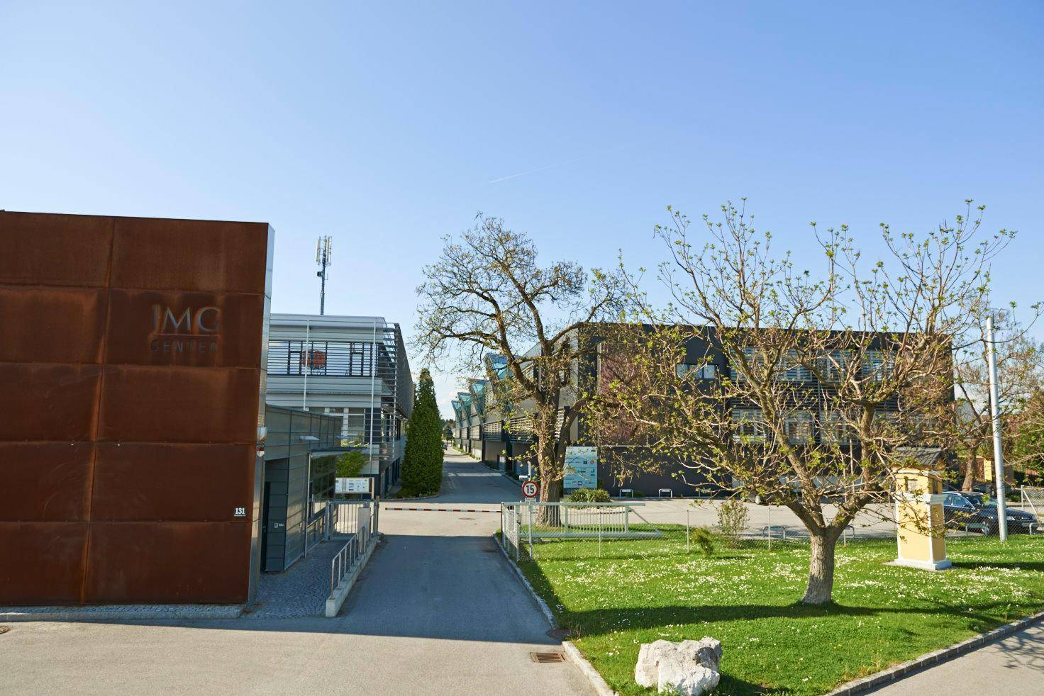Außenansicht eines Gewerbeparks mit mehreren Gebäuden, Bäumen und einer Zufahrt unter klarem Himmel.