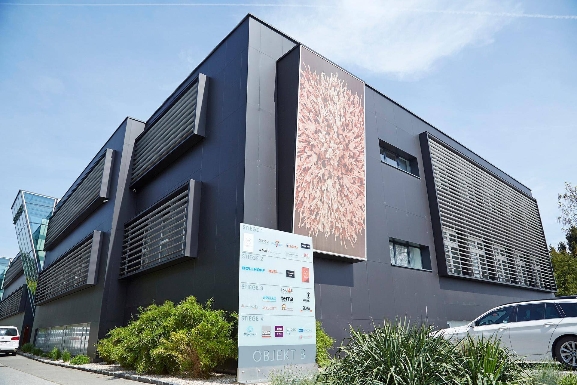 Modernes Geschäftsgebäude mit dunkler Fassade, großen Fenstern und Außenwerbung unter blauem Himmel.