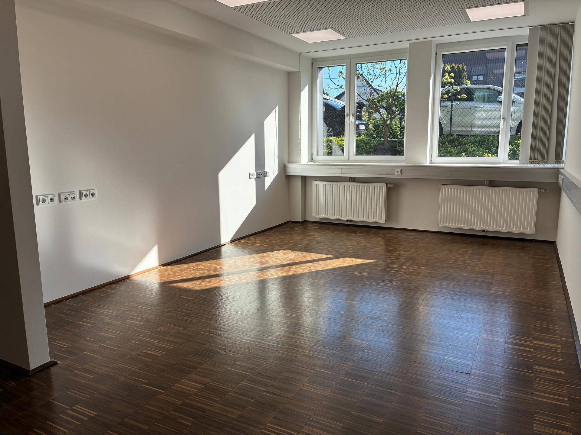 Helles, leeres Büro mit großen Fenstern, Holzboden und Heizkörpern, bereit zur individuellen Gestaltung.