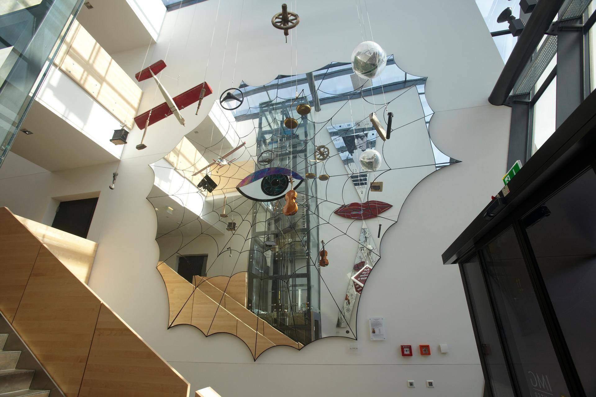 Beeindruckende Eingangshalle mit hoher Decke, dekorativer Kunstinstallation und einem Aufzug im Hintergrund.
