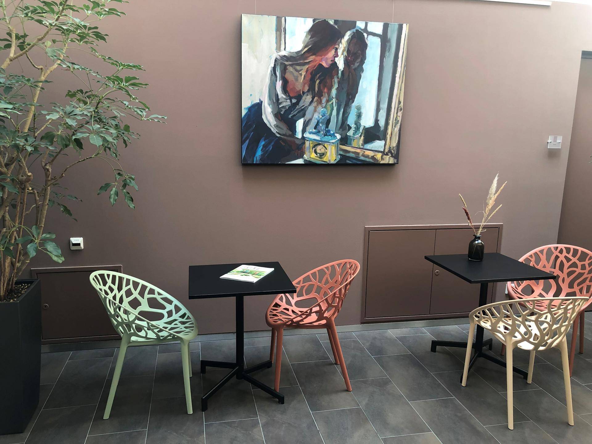 Moderner Loungebereich mit kleinen Tischen, farbigen Stühlen und einem Kunstwerk an der Wand.