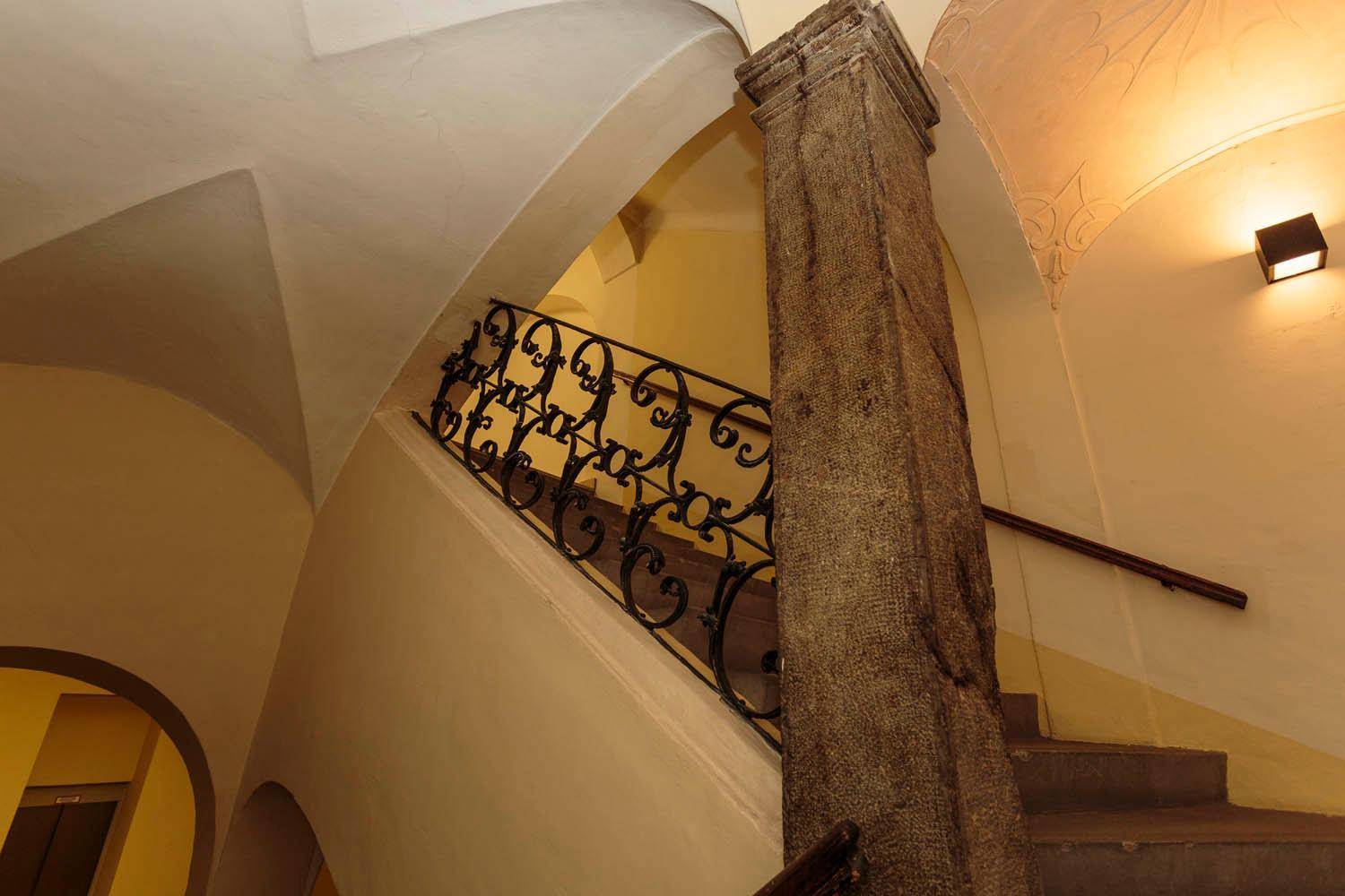 Historisches Treppenhaus mit massiven Steinsäulen, schmiedeeisernem Geländer und gewölbten Decken.