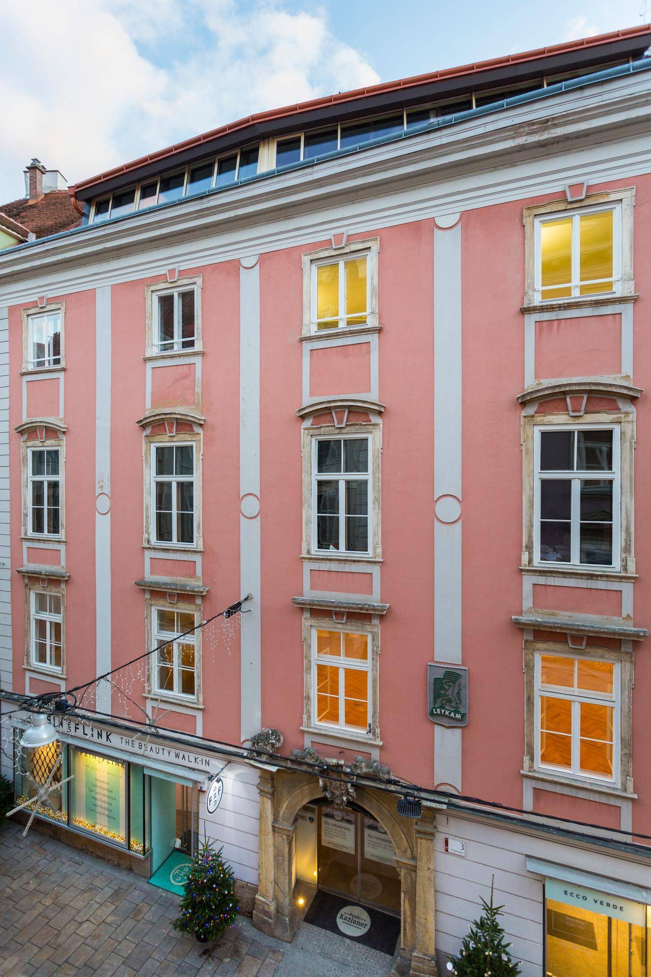 Historische rosa Fassade eines Gebäudes mit vielen Fenstern und dekorativen Elementen in der Abenddämmerung.