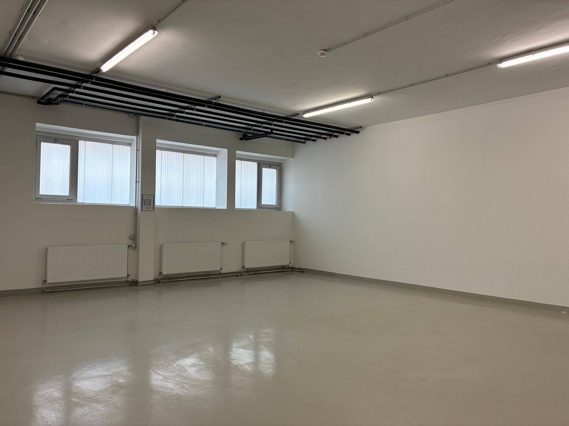 Heller Büroraum mit großen Fenstern, weißen Wänden und funktionaler Beleuchtung an der Decke.