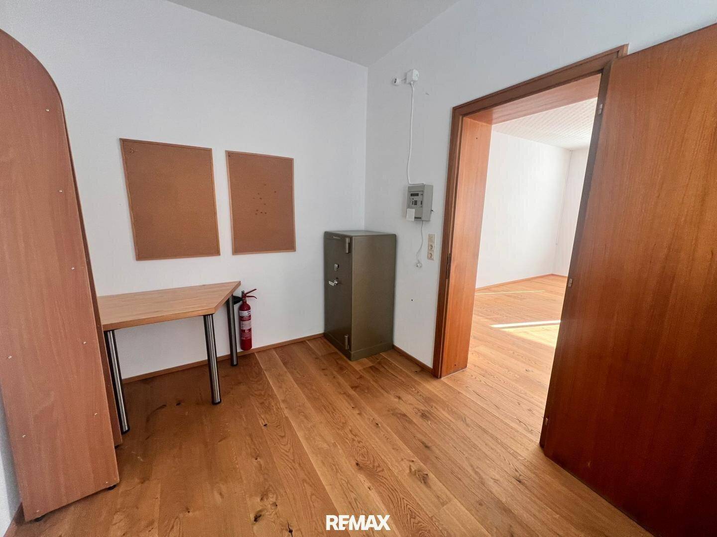 Kleiner Büroraum mit Holzboden, einem Safe und einer Pinnwand, ideal für Lagerung oder Einzelbüro.