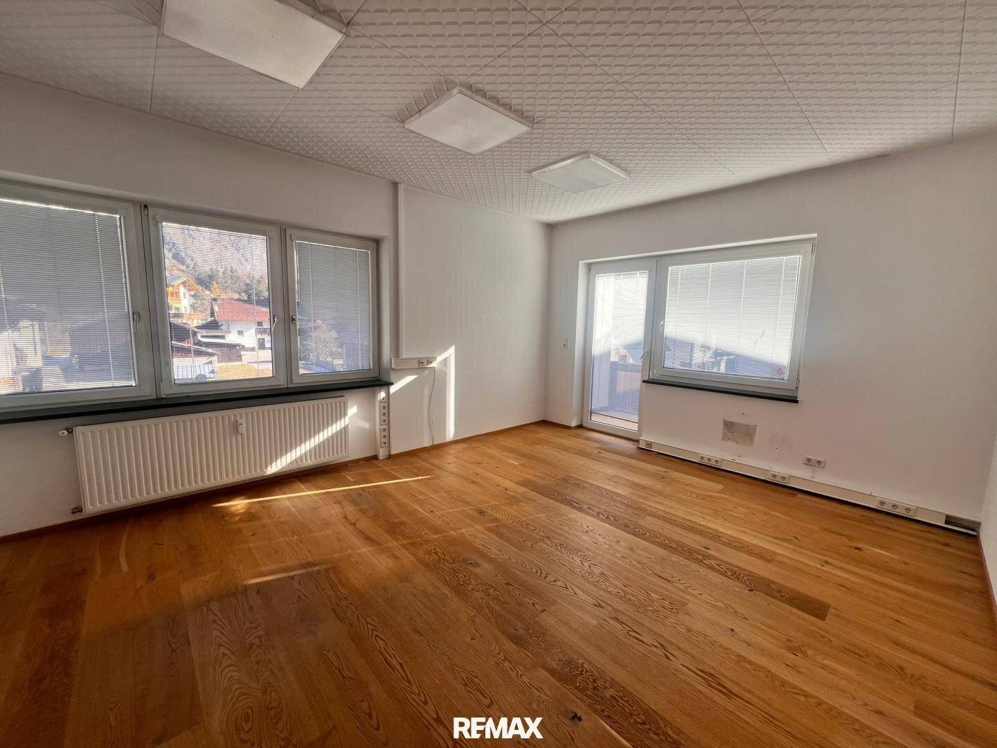 Heller Büroraum mit Holzboden, großen Fenstern und Zugang zu einem Außenbereich, ideal für Arbeitsplätze.