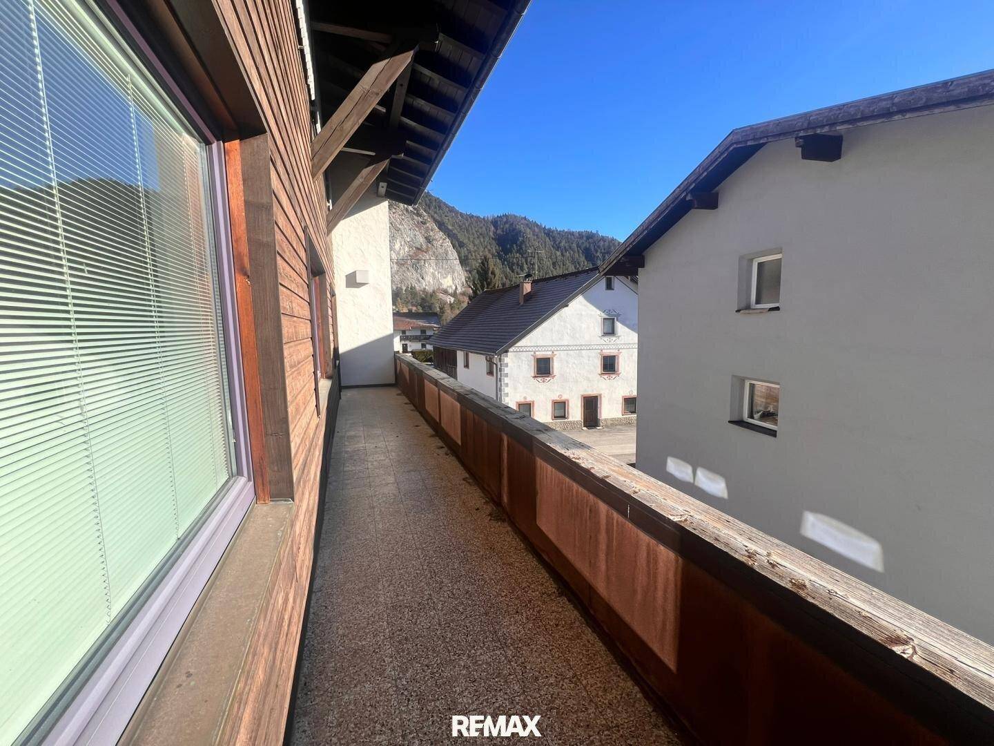 Langer Balkon mit Holzboden und Blick auf die umliegenden Häuser und Berge.