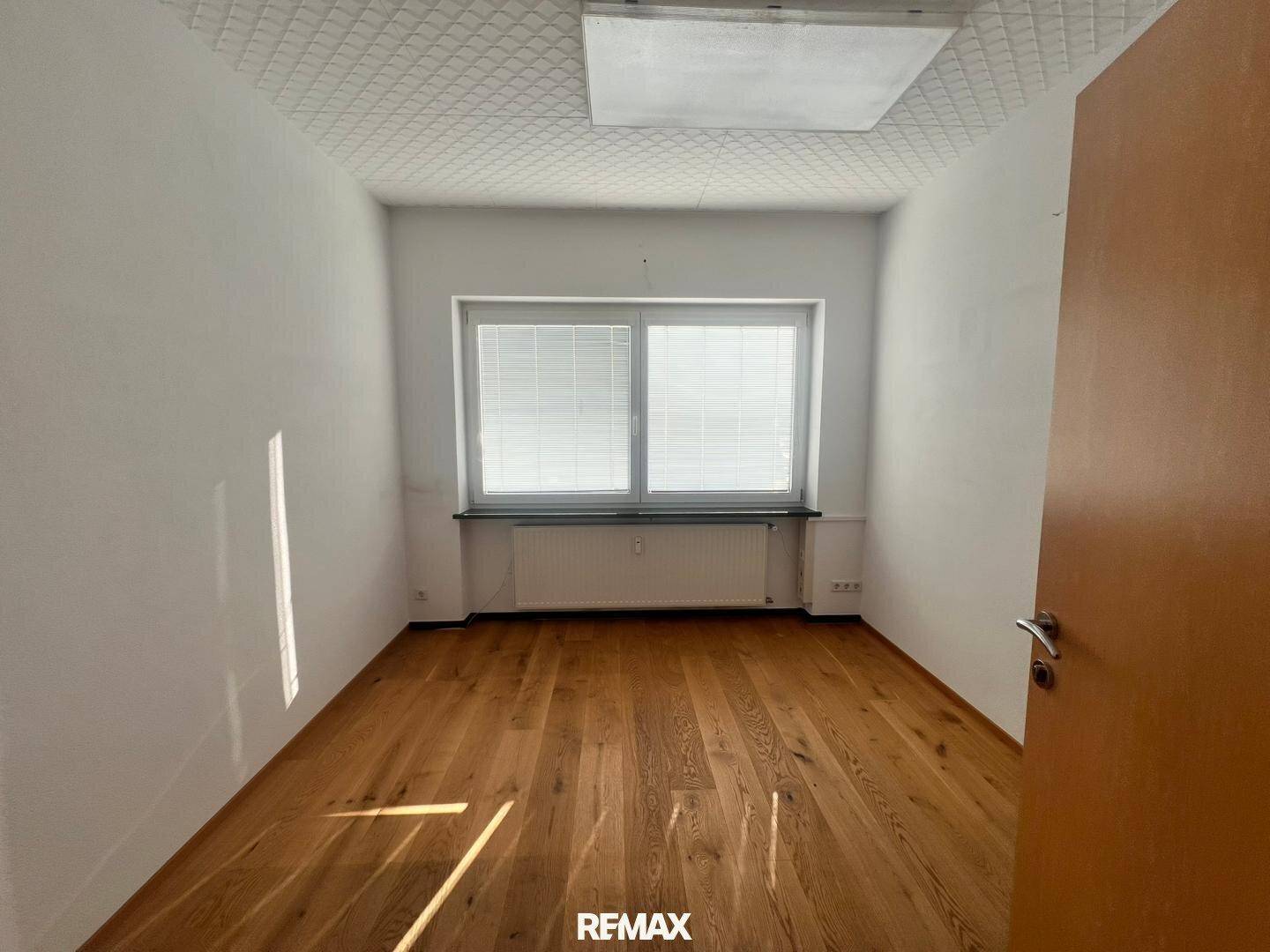 Kleinerer Büroraum mit Holzboden und einem Fenster, das viel Tageslicht hereinlässt.