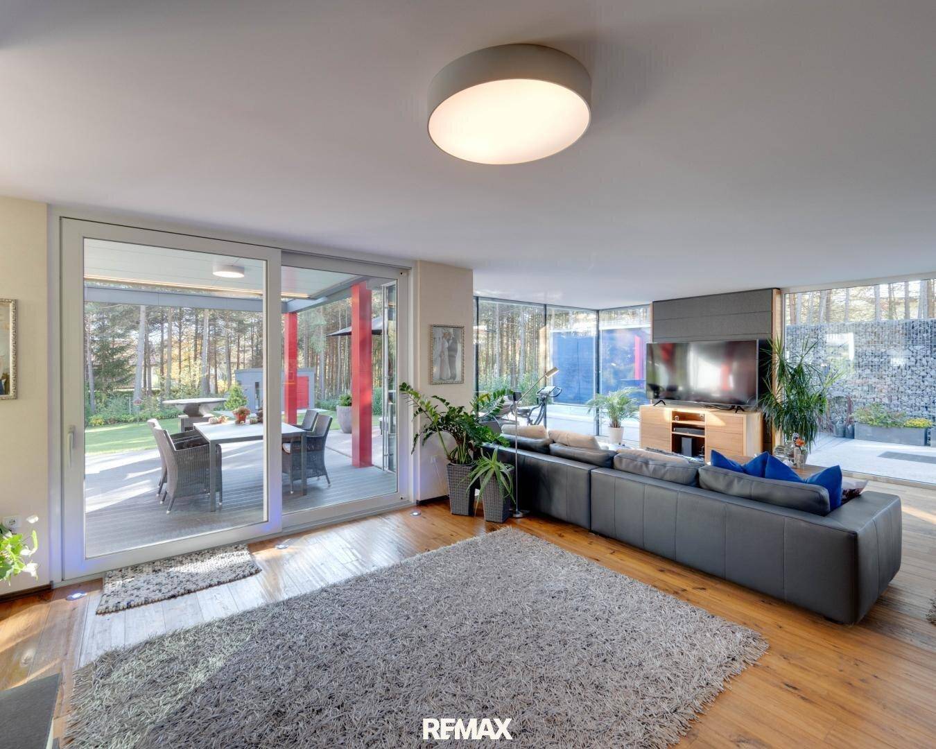 Helles Wohnzimmer mit Holzboden, großem Sofa und Zugang zur Terrasse mit Blick ins Grüne.