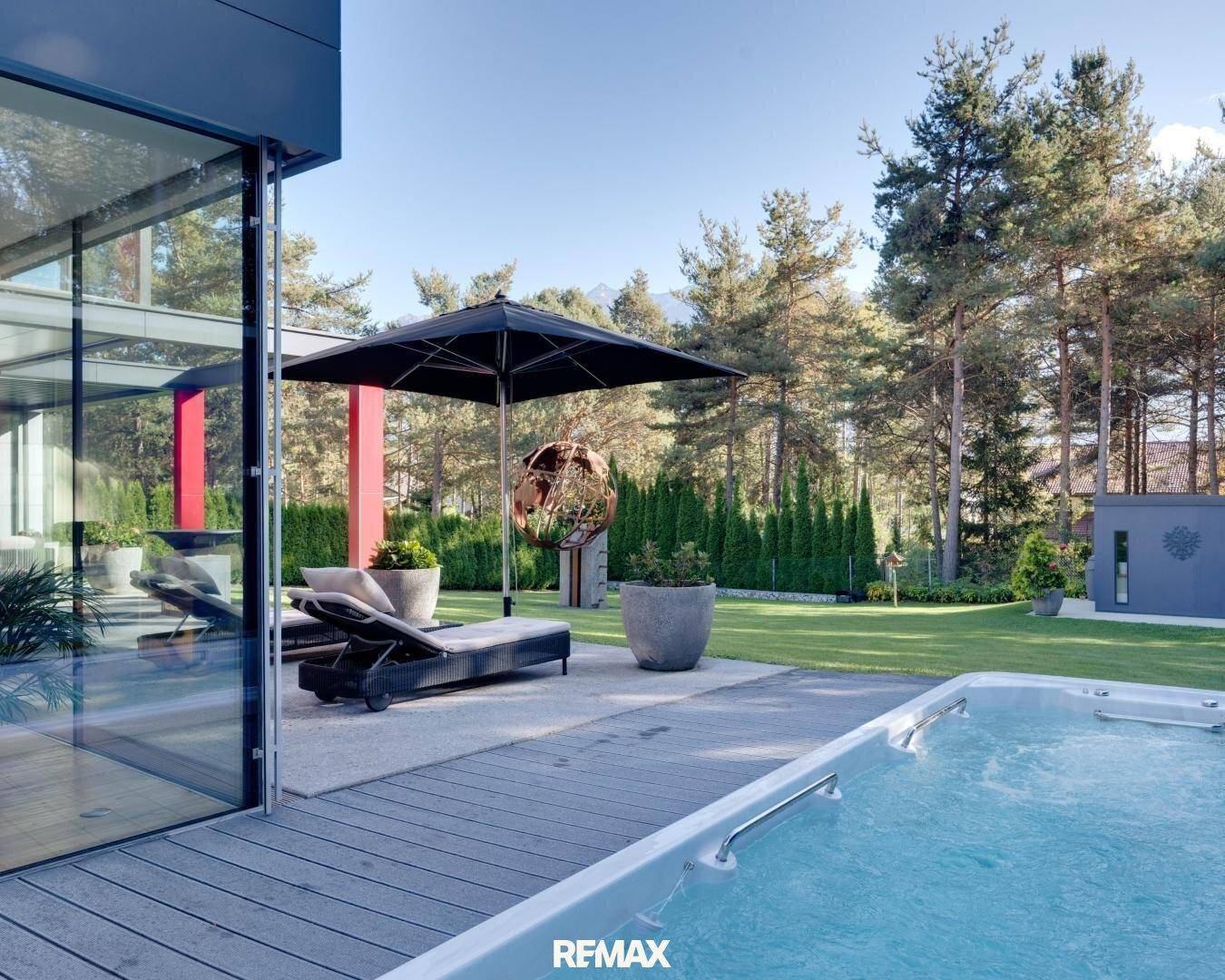 Moderner Terrassenbereich mit Whirlpool und raumhohen Glasfronten, die den Innenraum mit dem Garten verbinden.