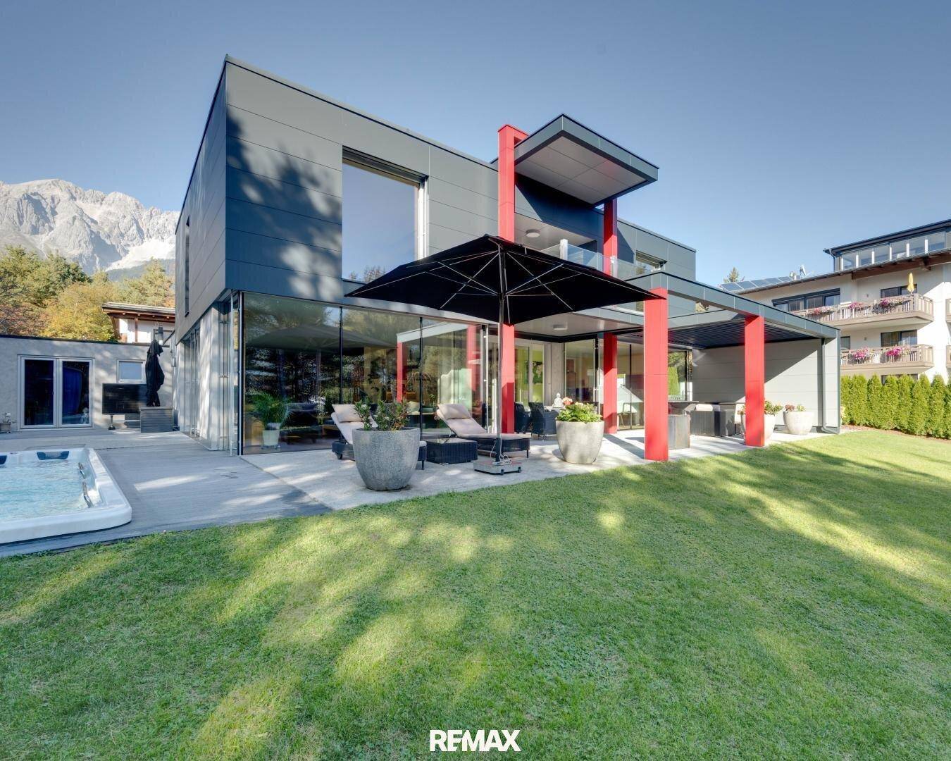 Moderne Villa mit weitläufigem Garten, großzügiger Terrasse, Pool und Whirlpool vor alpiner Kulisse.