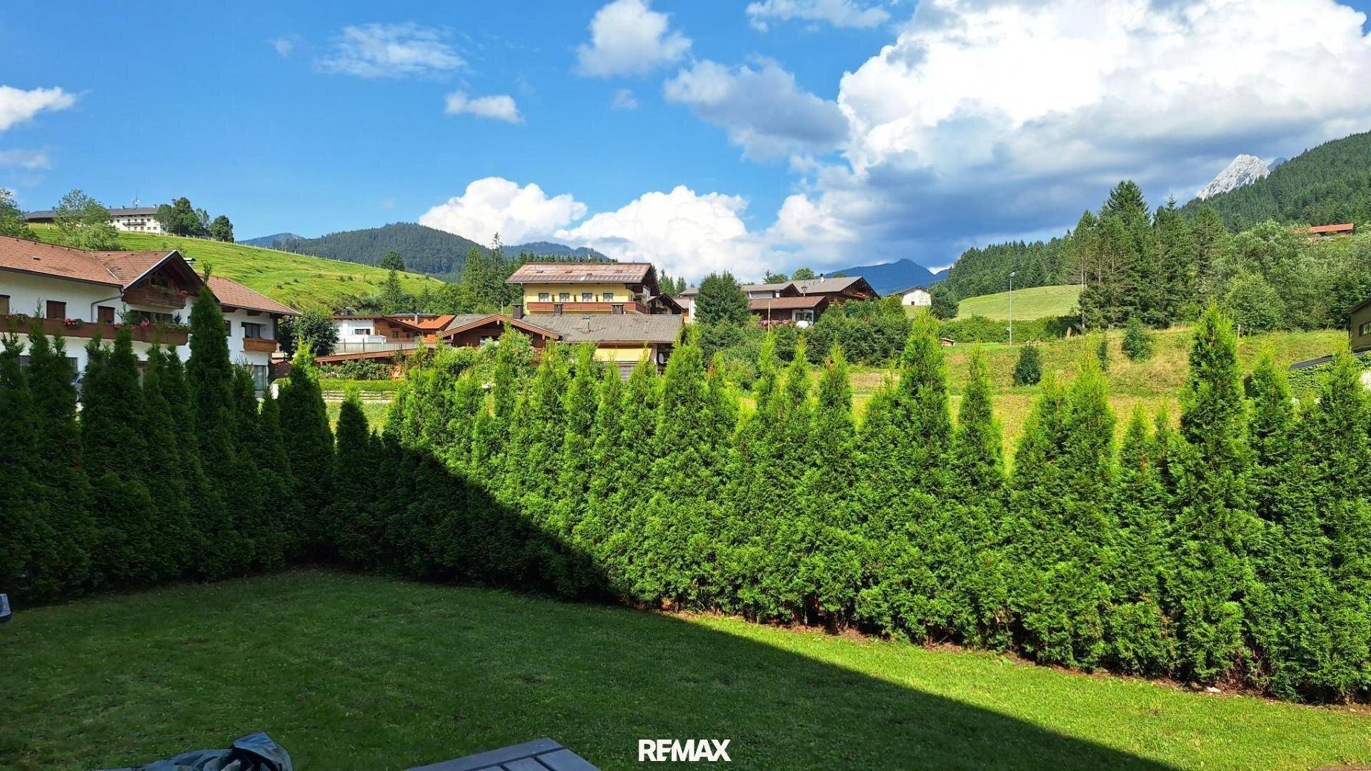 Gepflegter Gartenbereich mit Rasenfläche und hoher Hecke, bietet Privatsphäre und Bergblick.