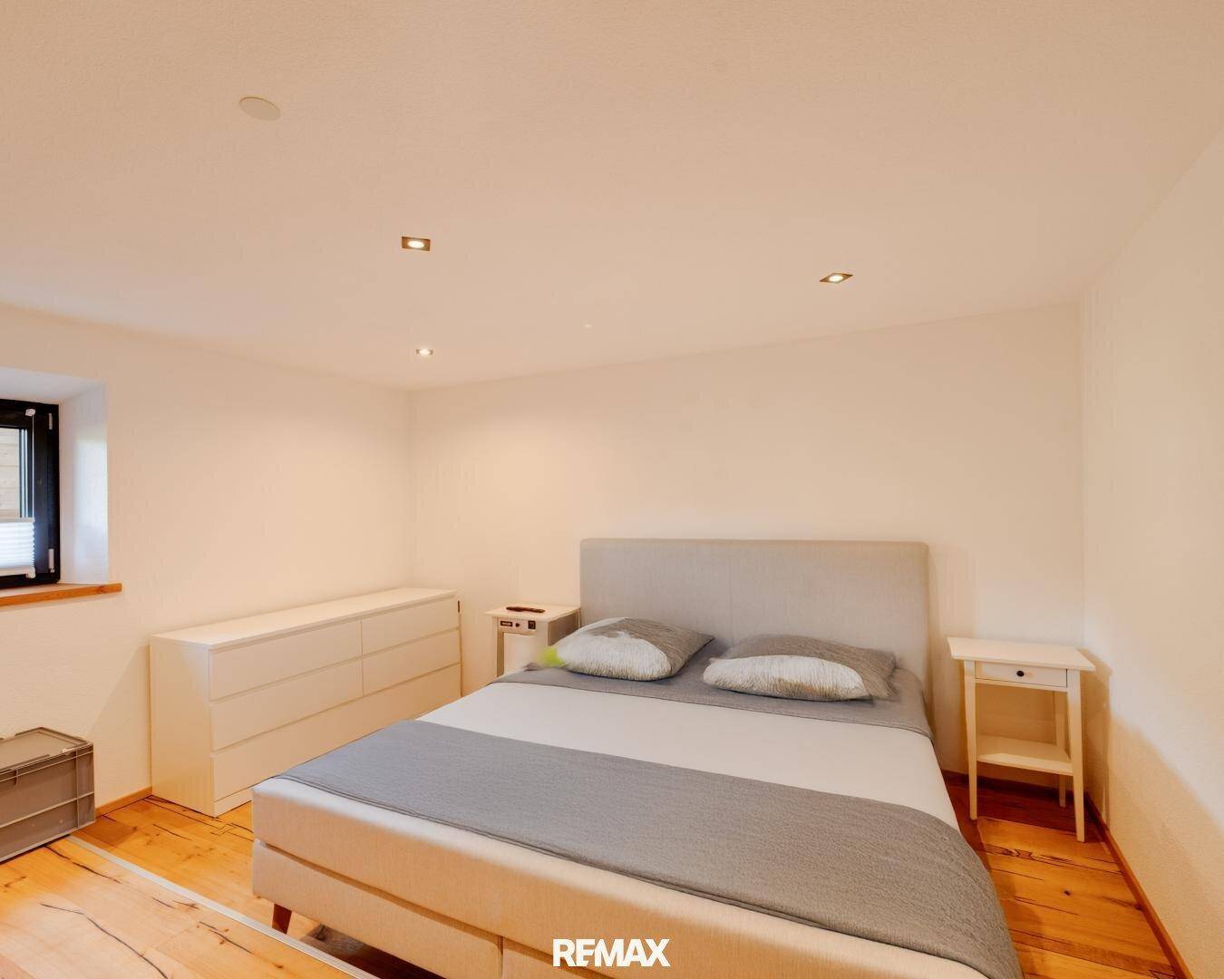 Helles Schlafzimmer mit Doppelbett, weißer Kommode und warmem Holzboden, einladend gestaltet.
