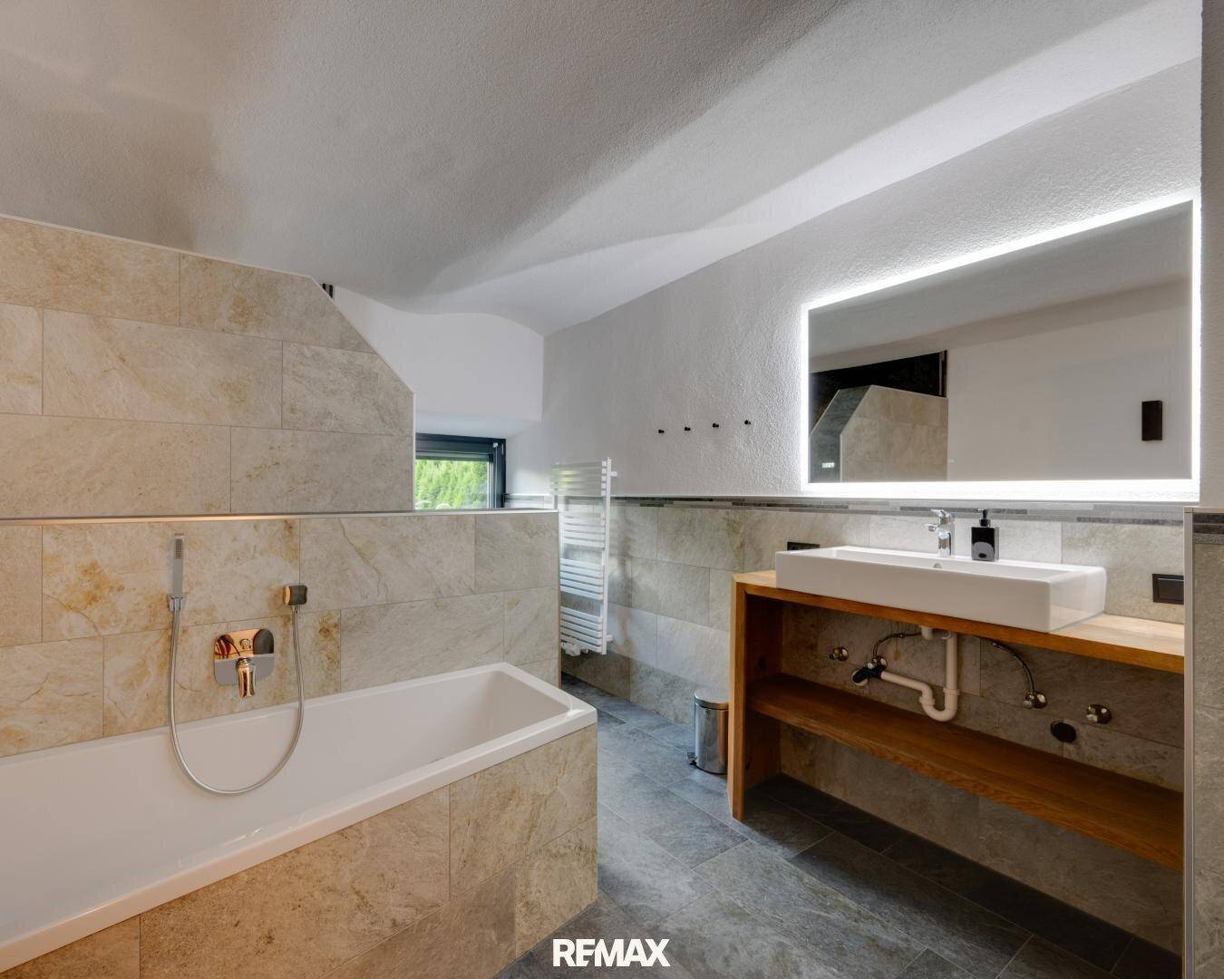 Modernes Badezimmer mit Badewanne, stilvollem Waschtisch und beleuchtetem Spiegel.