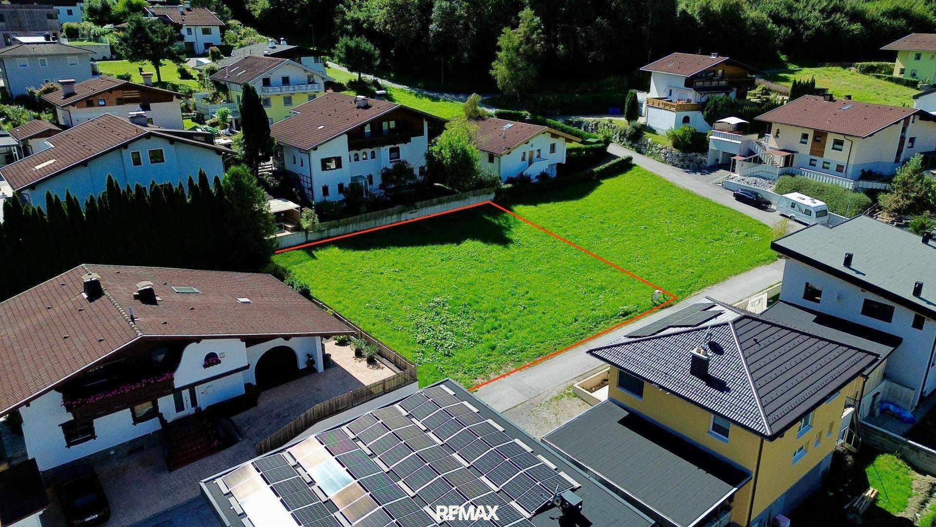 Luftaufnahme des Baugrundstücks in einer Wohnsiedlung mit Blick auf die umliegende Berglandschaft.