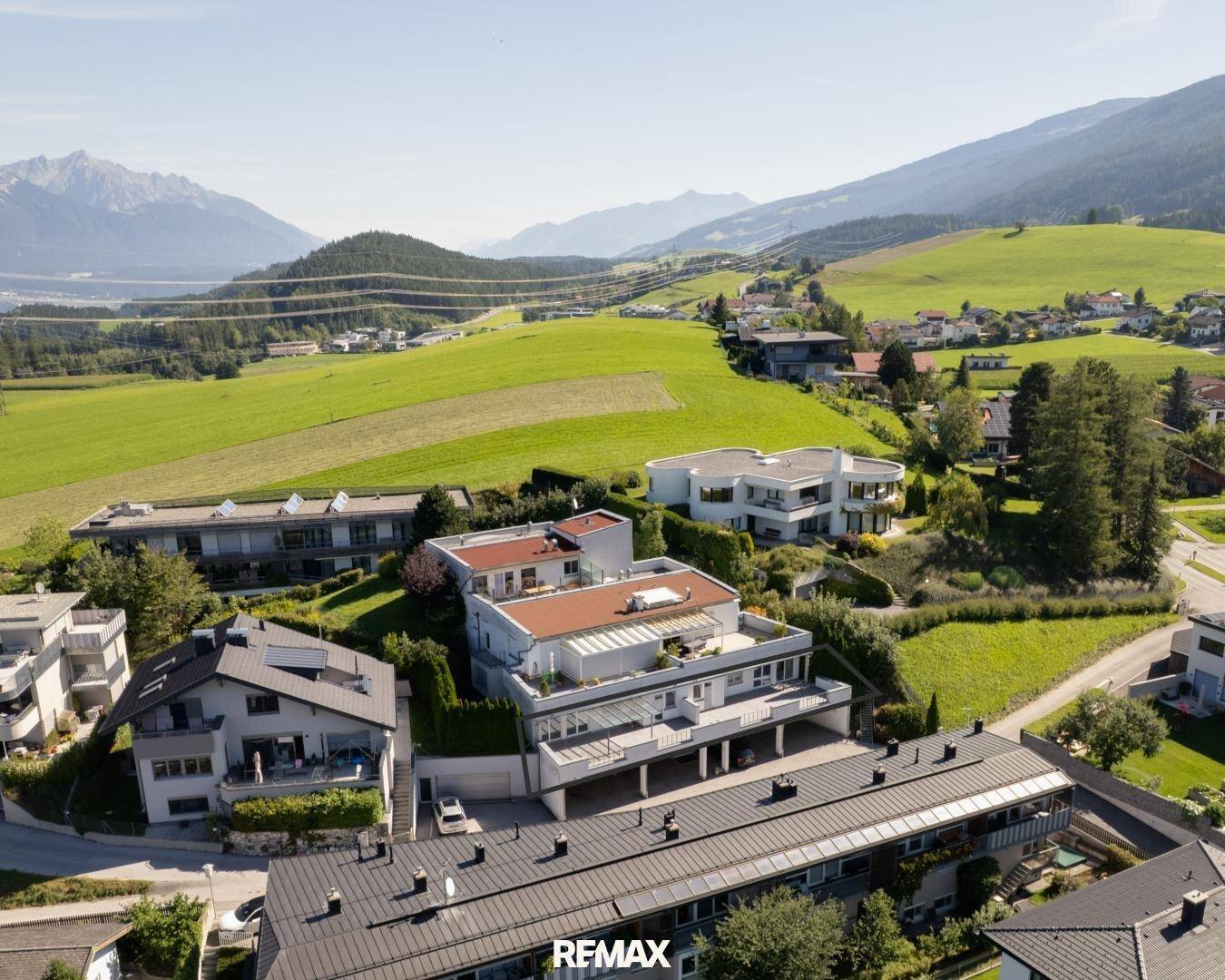 Panoramablick auf eine Wohngegend eingebettet in grüne Hügel mit fernen Berggipfeln.