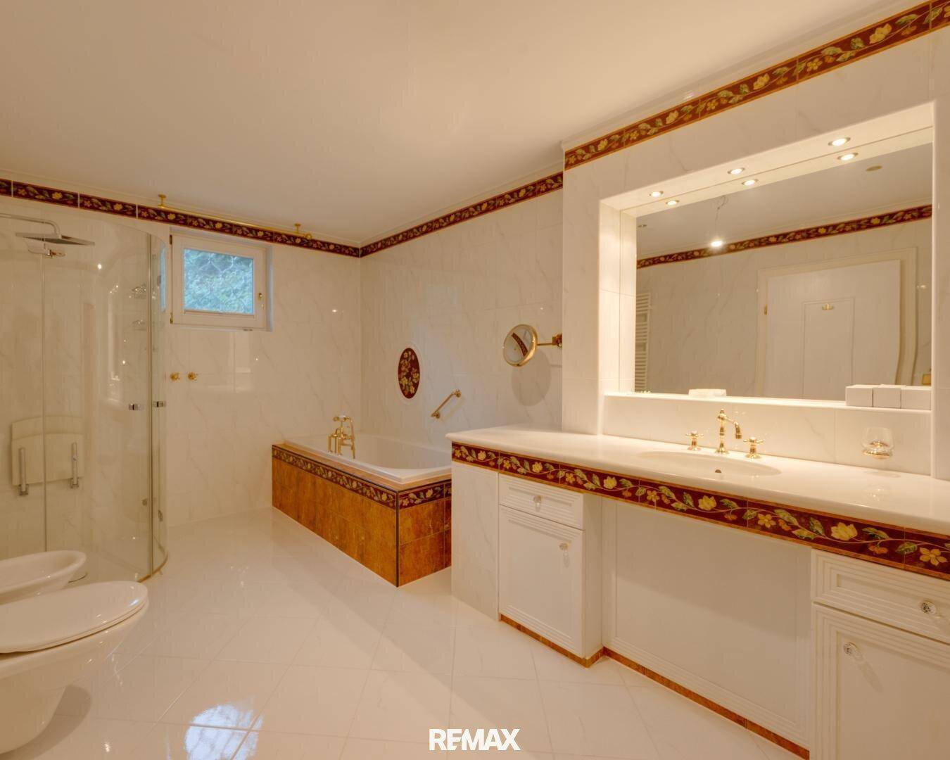 Elegantes Badezimmer mit Marmorfliesen, goldfarbenen Armaturen, Badewanne und separater Dusche.