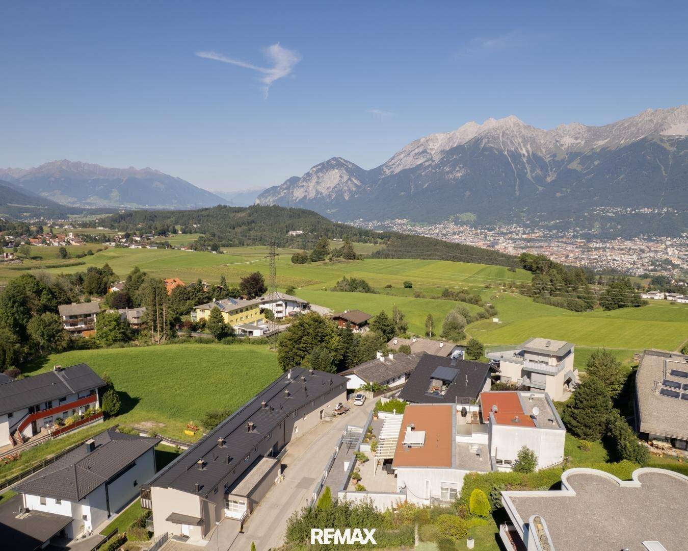 Luftaufnahme einer Wohngegend mit weiten Grünflächen und Blick auf die Stadt und Berge.