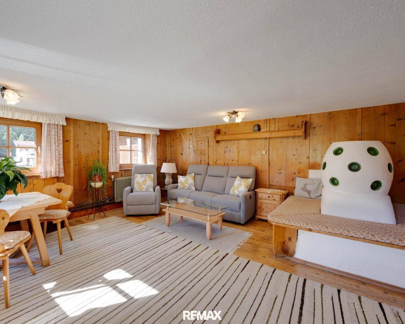 Gemütliches Wohnzimmer im alpinen Stil mit Holzvertäfelung, Kachelofen und bequemen Sitzmöbeln.
