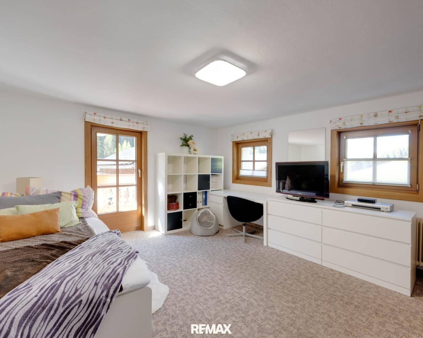 Helles Schlafzimmer mit Teppichboden, Kommode und Zugang zu einem Balkon.