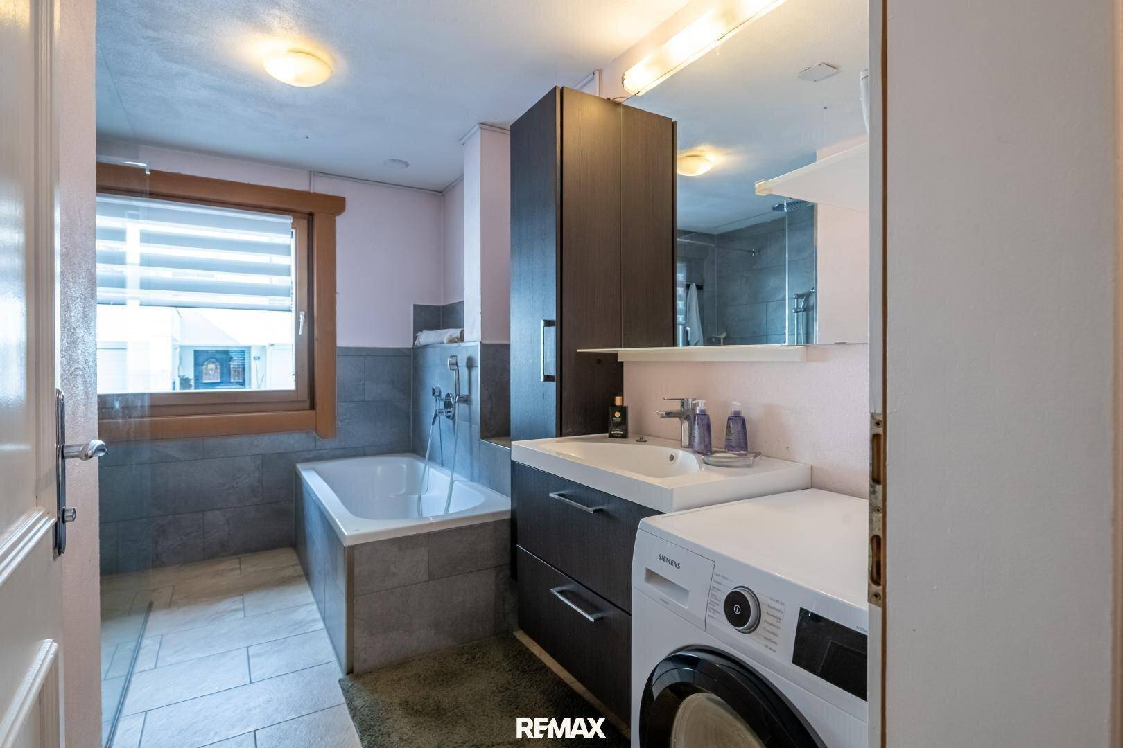 Praktisches Badezimmer mit Badewanne, Waschbecken und integrierter Waschmaschine.