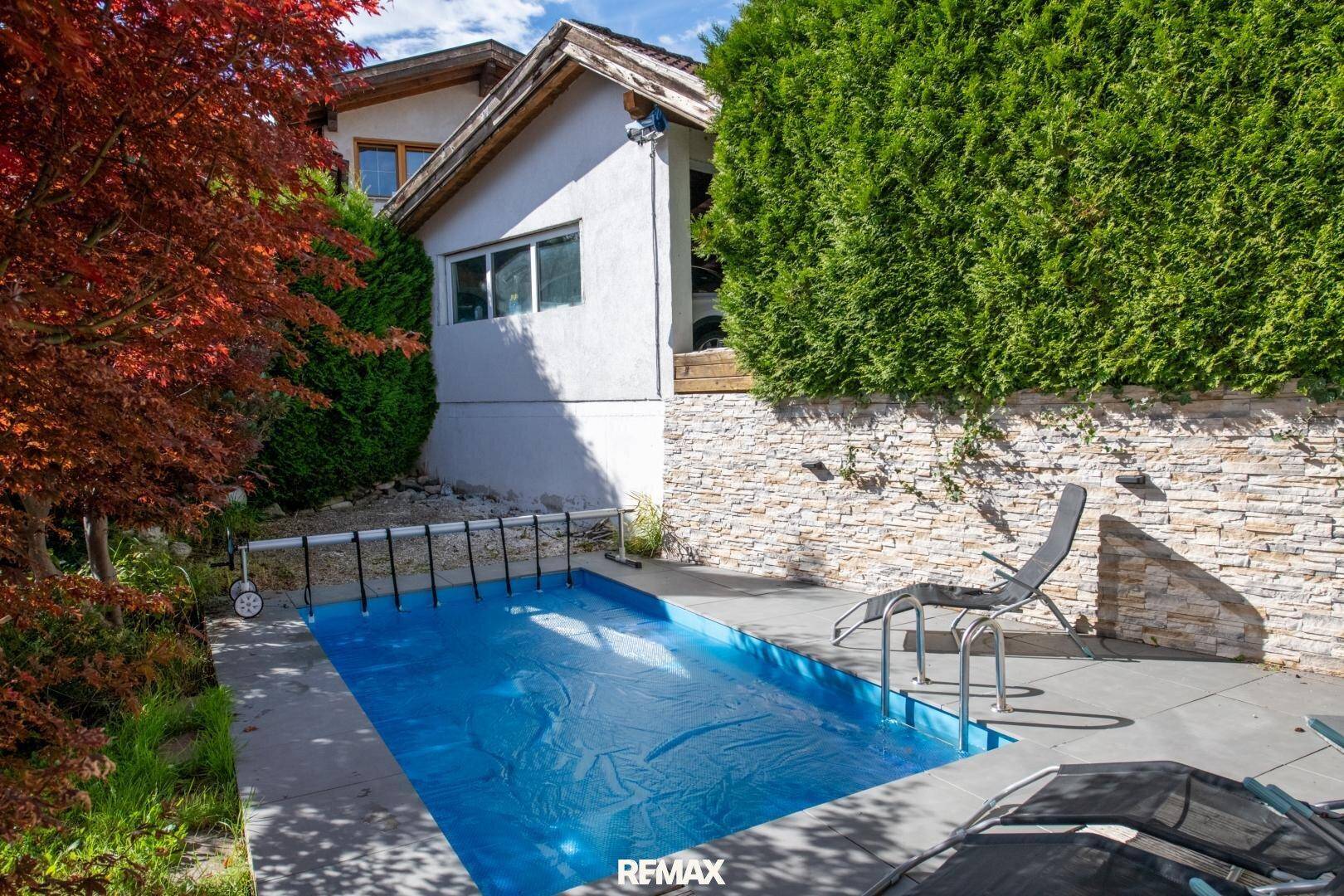 Eingezäunter Poolbereich mit Steinmauer und Hecke, ideal für Entspannung im Freien.